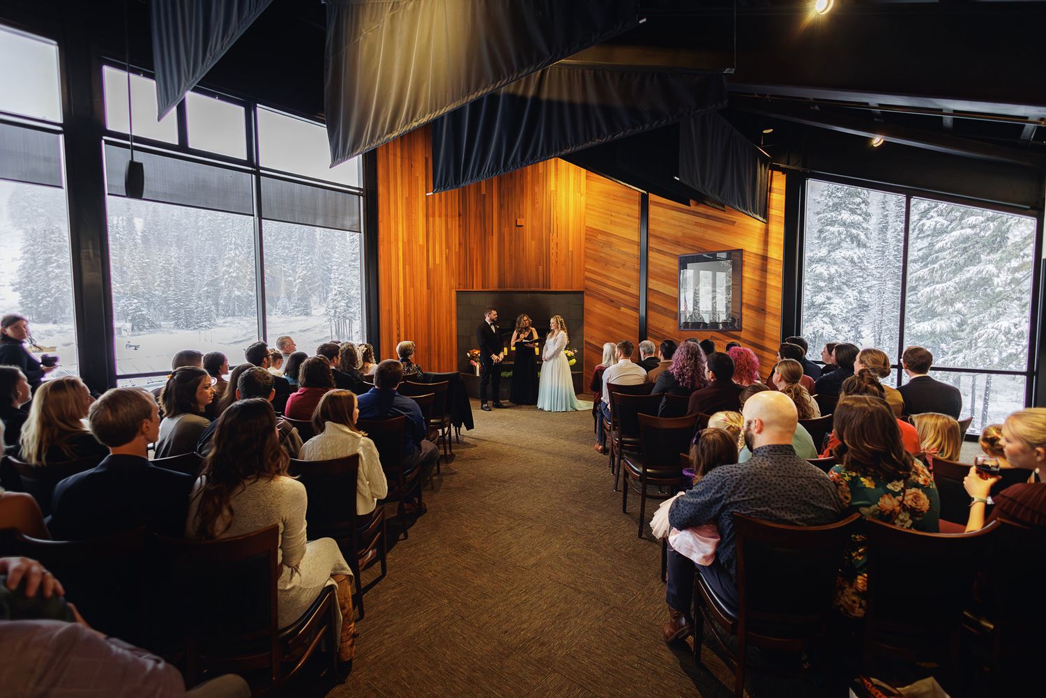 A group of people attend a conference or meeting in a modern room with large windows overlooking a snowy landscape.