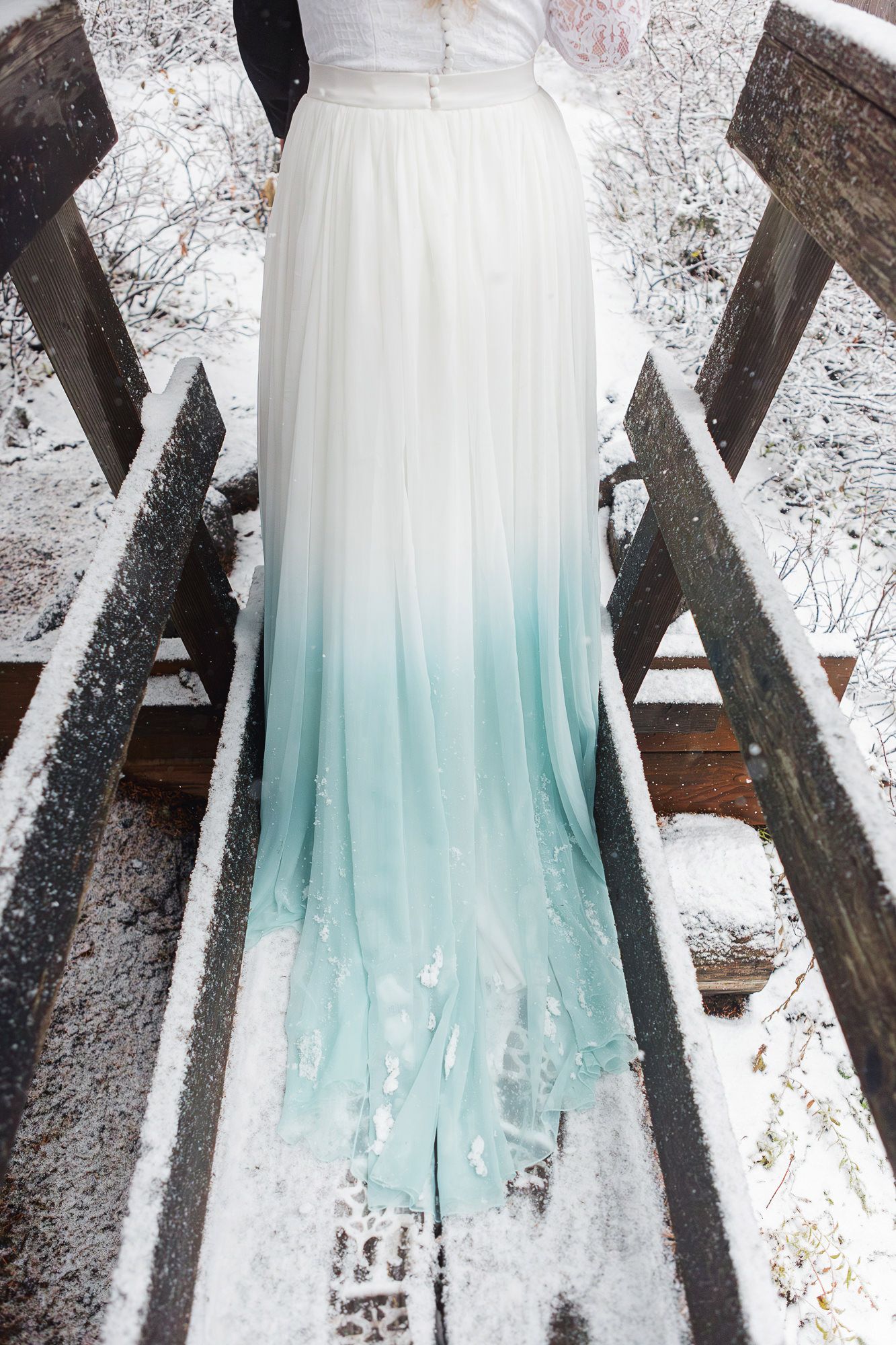 A white wedding dress with an ombre effect fading into mint green at the bottom hangs against a snowy winter backdrop.