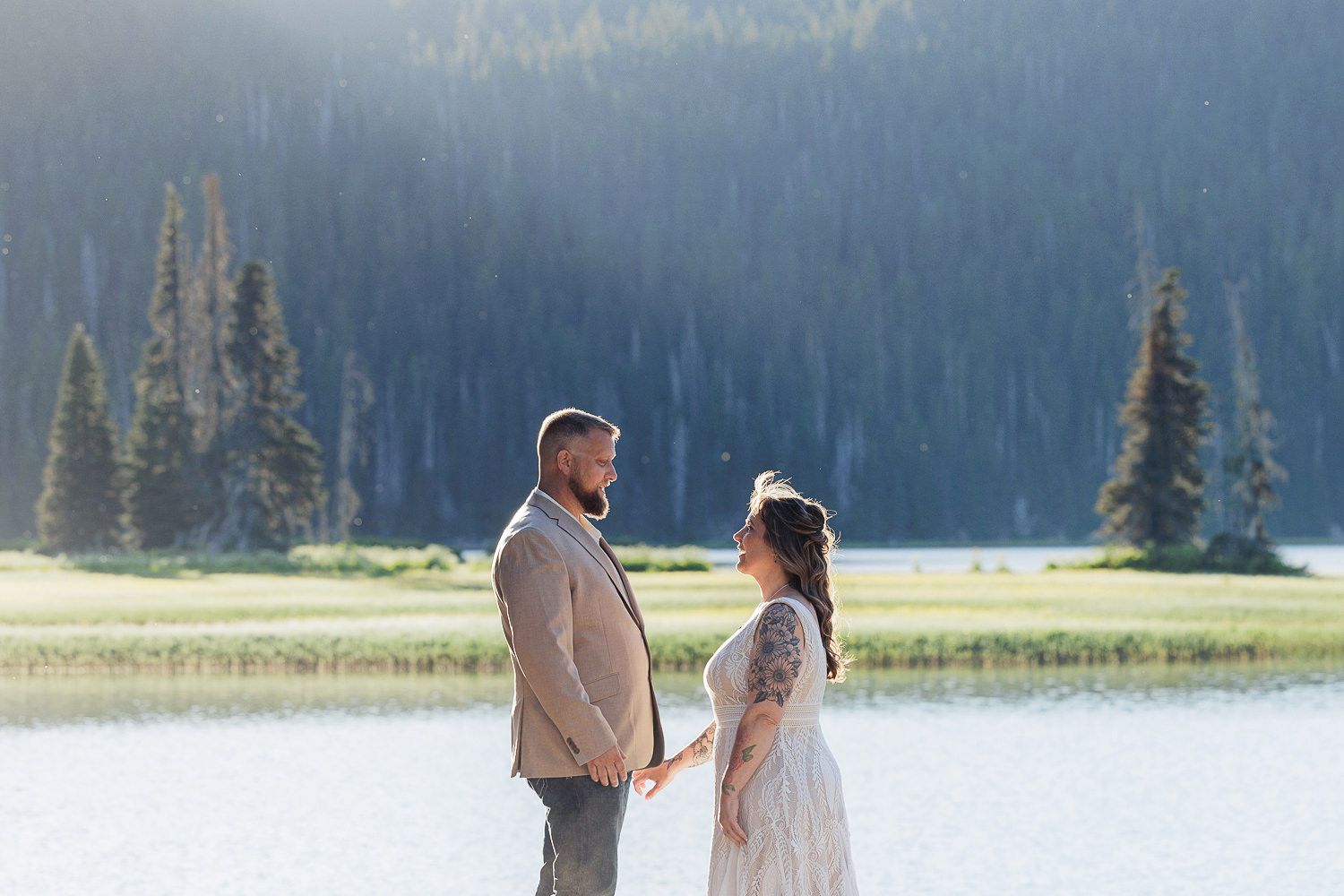 A couple exchanges vows during a romantic lakeside wedding ceremony against a backdrop of mountains and forests.