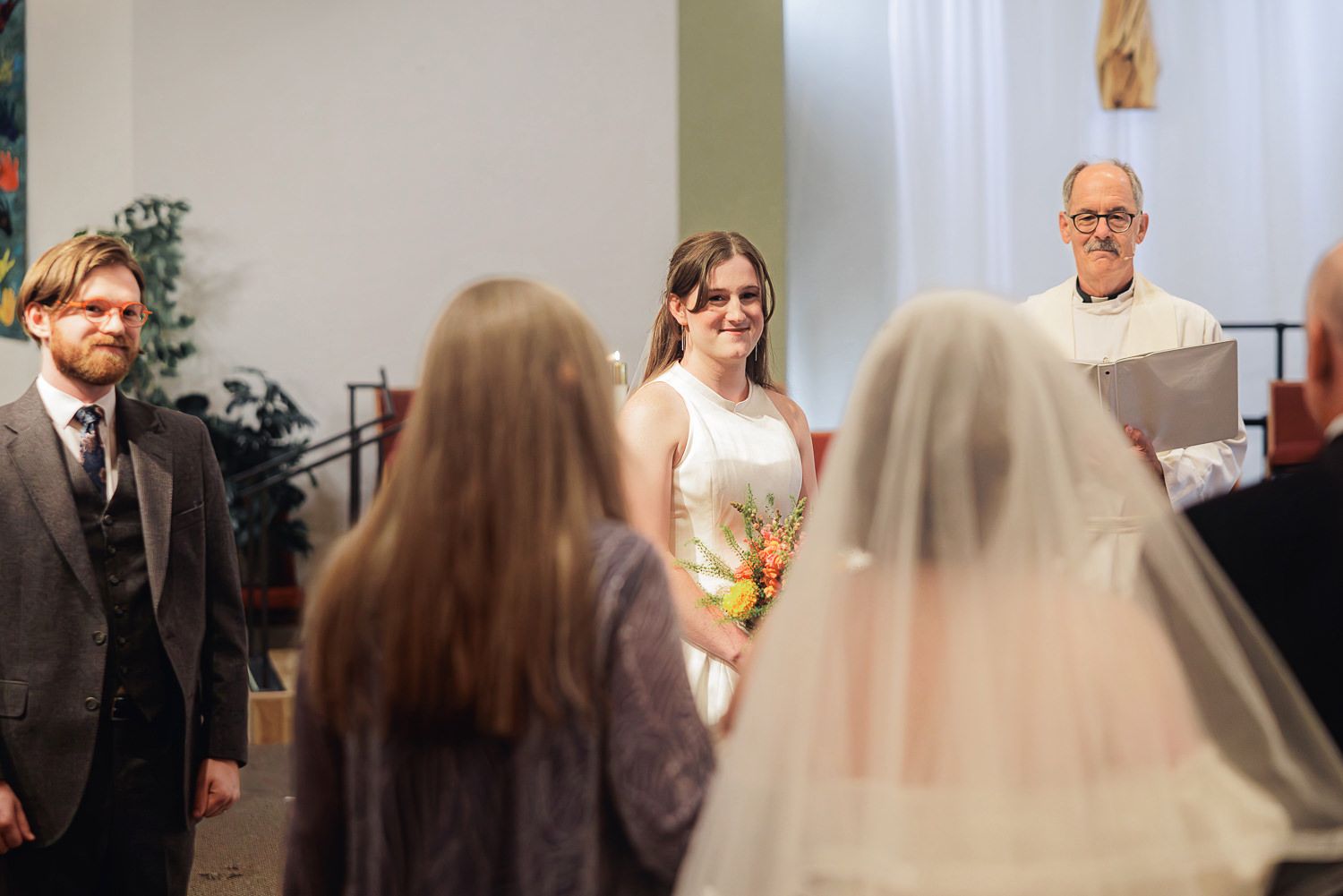 A wedding ceremony in progress with guests seated in church pews as the couple stands at the altar.