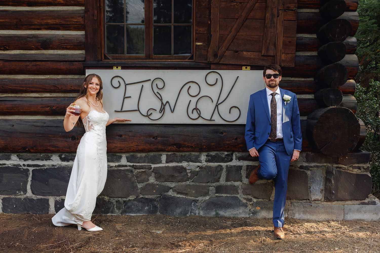A couple poses playfully on rustic wooden steps outside a log cabin during a wedding photoshoot.