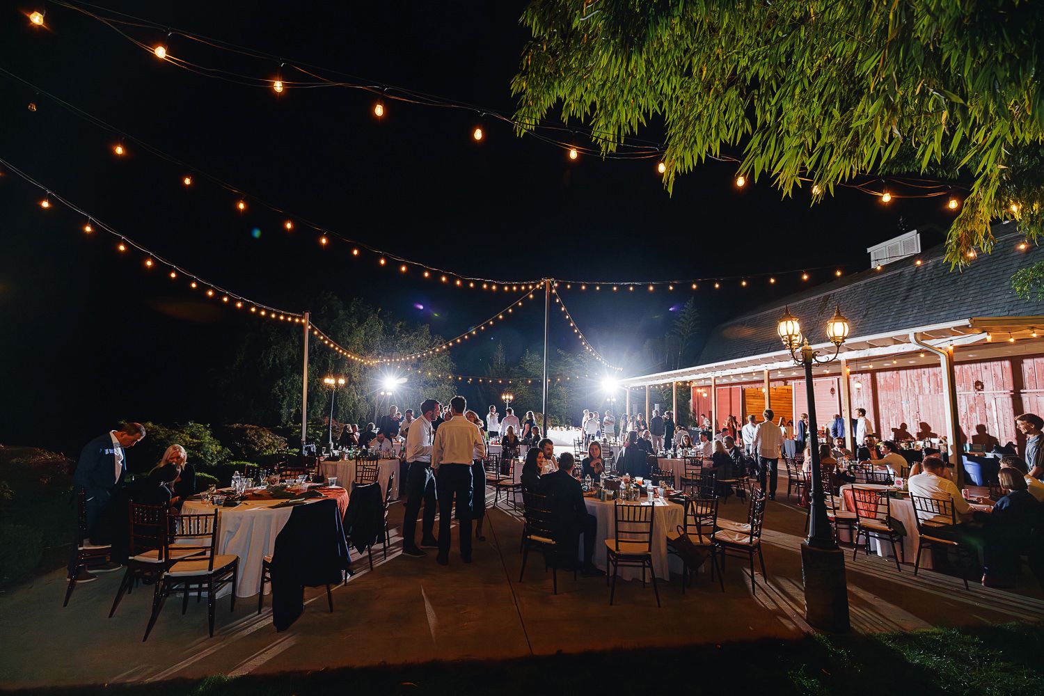 String lights illuminate an outdoor evening market with vendor stalls and people browsing under a dark night sky.