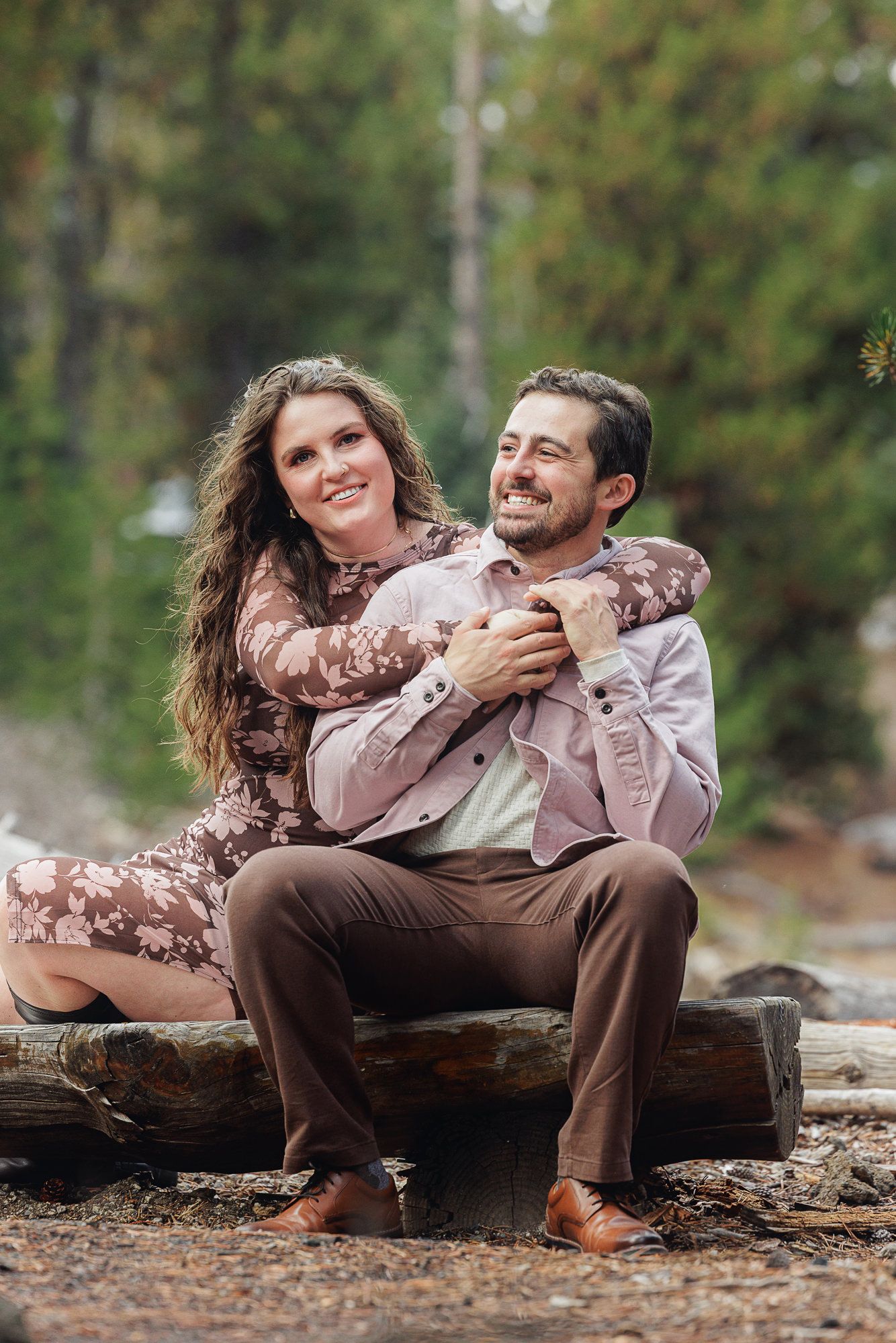 Romantic couple in coordinating brown outfits share playful moments while sitting on a wooden bench in nature.