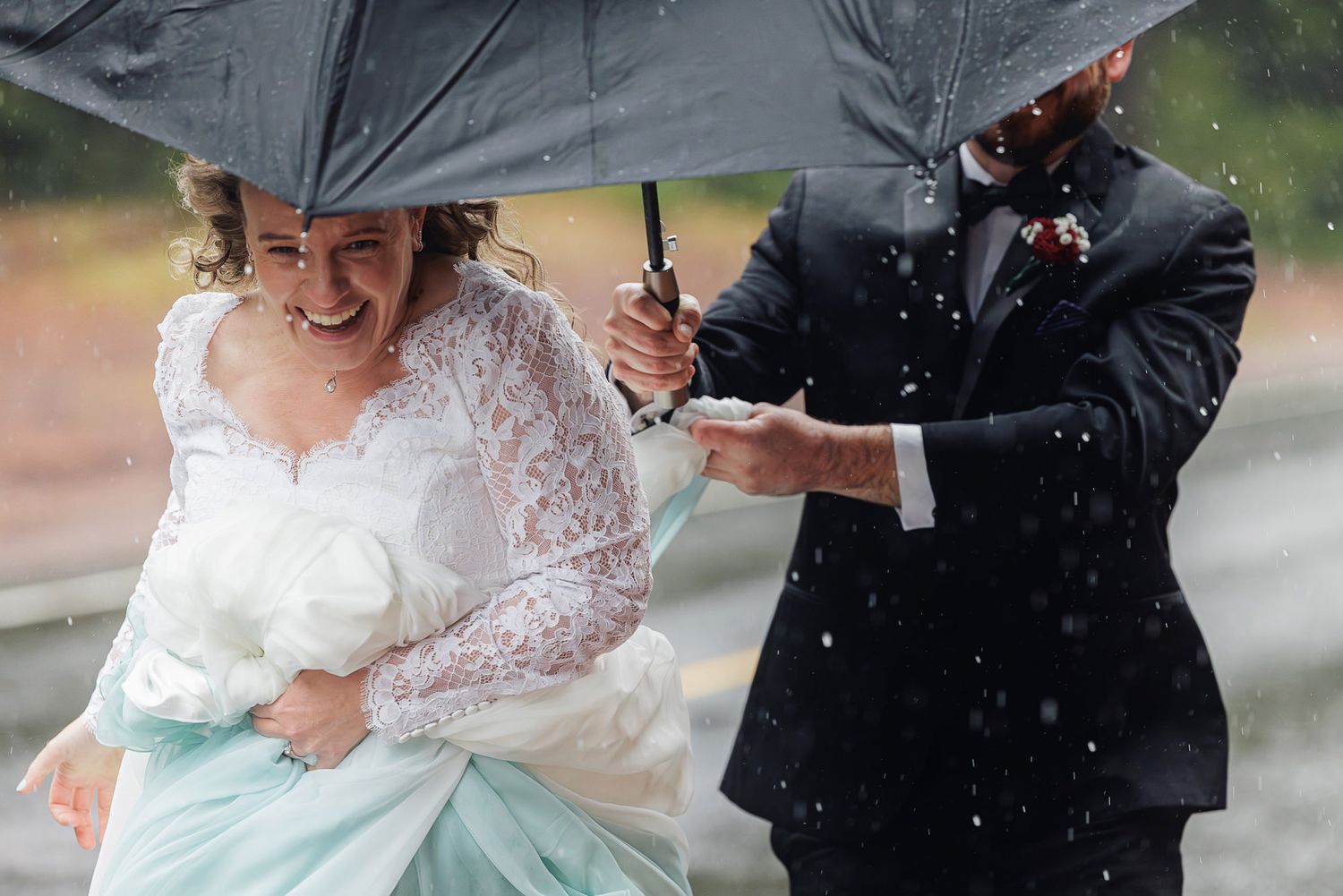 A couple shares an umbrella in the rain while wearing wedding attire during their outdoor celebration.