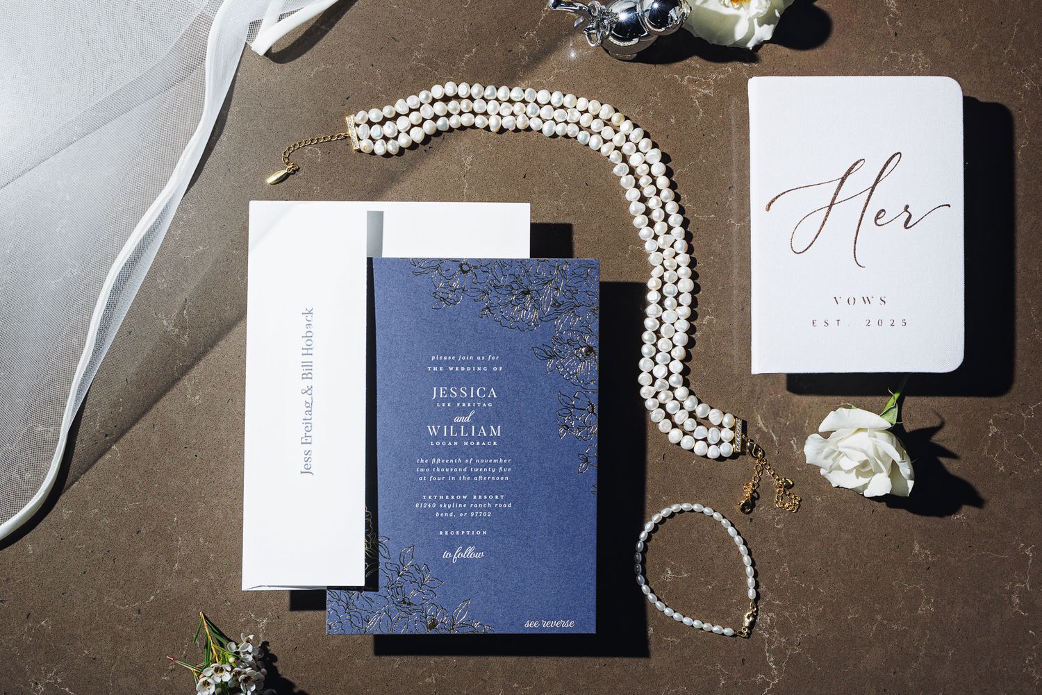 Wedding invitation suite featuring navy blue and white cards with elegant calligraphy and pearl necklace details.