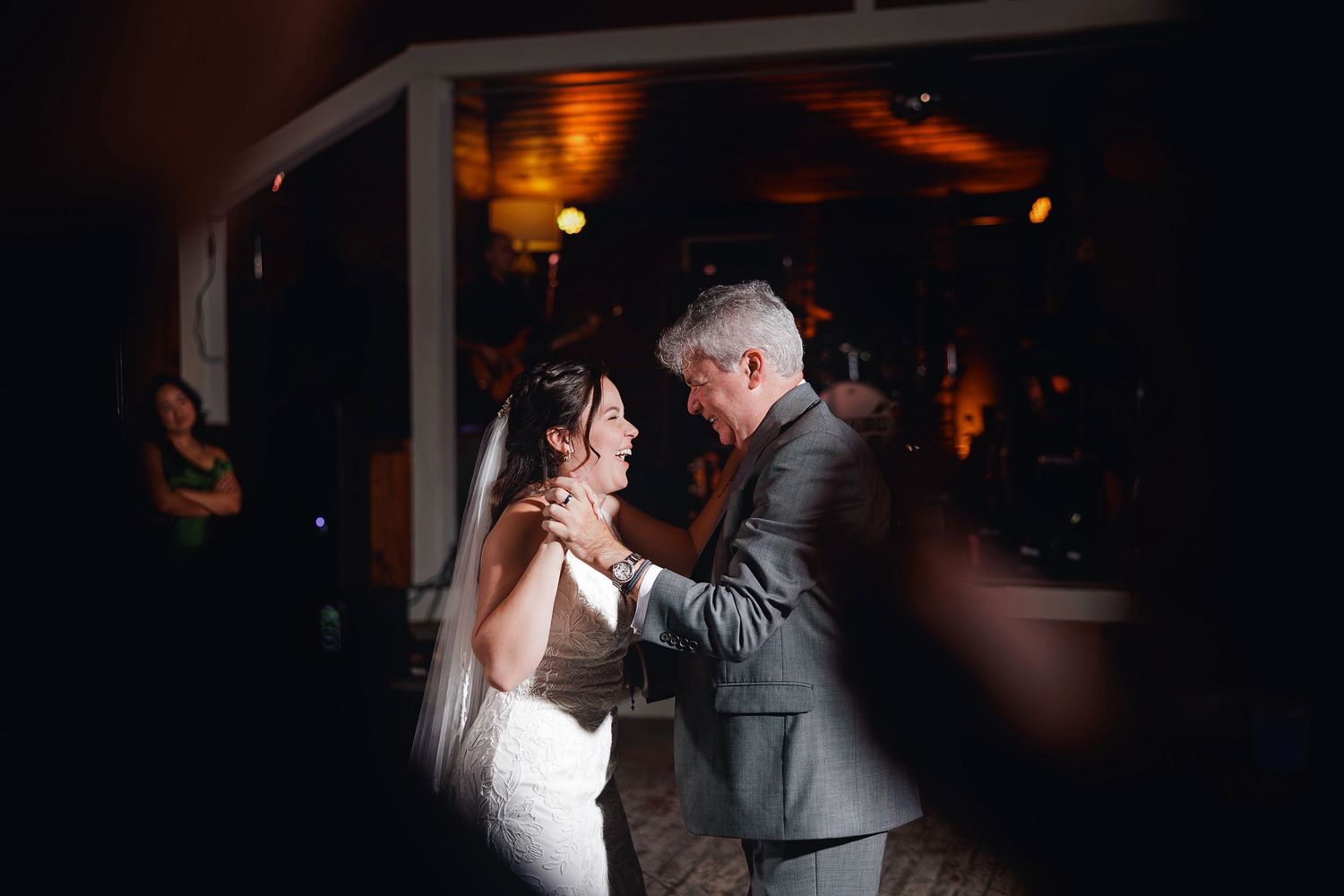 Bride and father share an emotional first dance at a dimly lit wedding reception venue.
