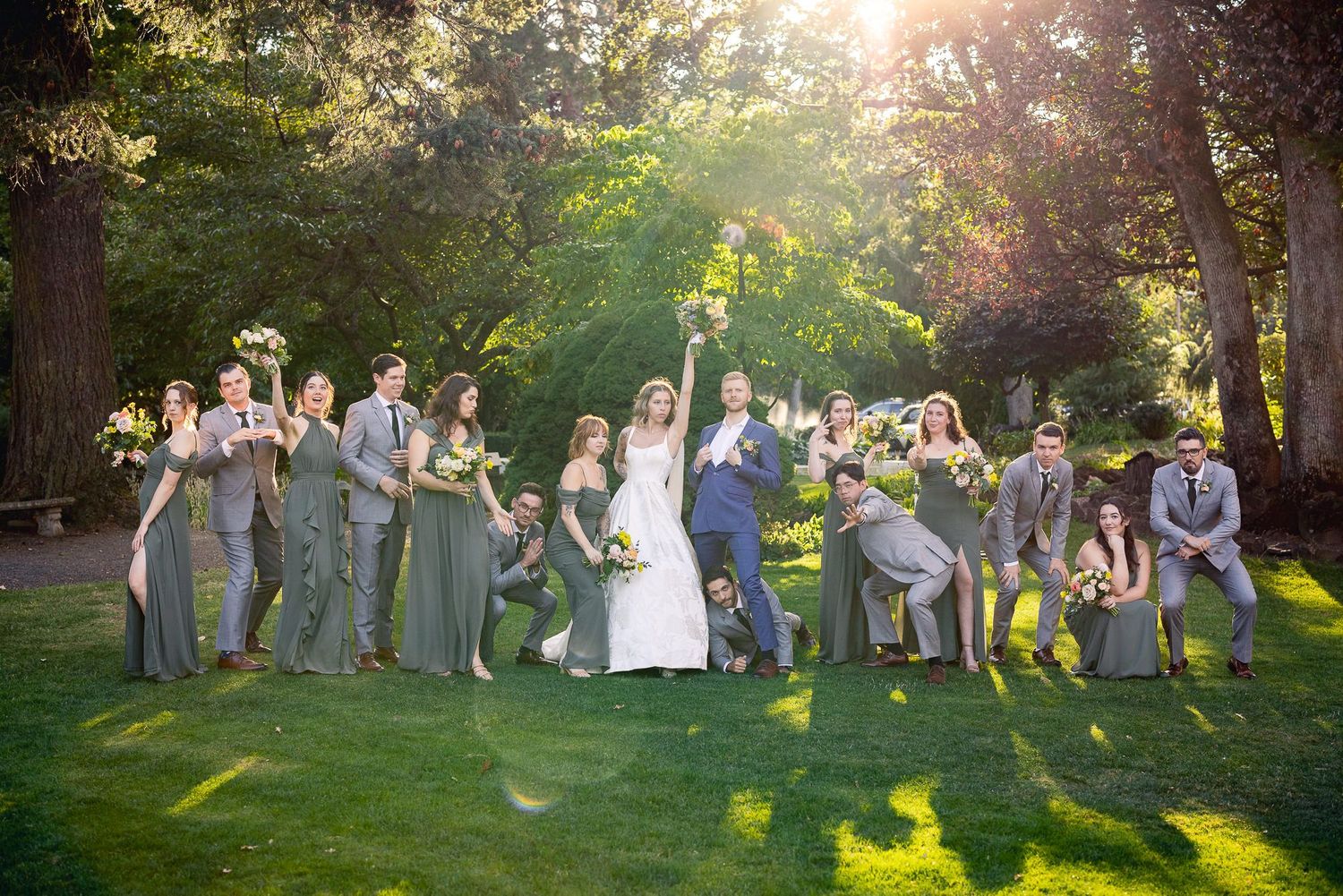 Wedding party in grey attire poses on sunlit grass with trees casting golden evening light and shadows.
