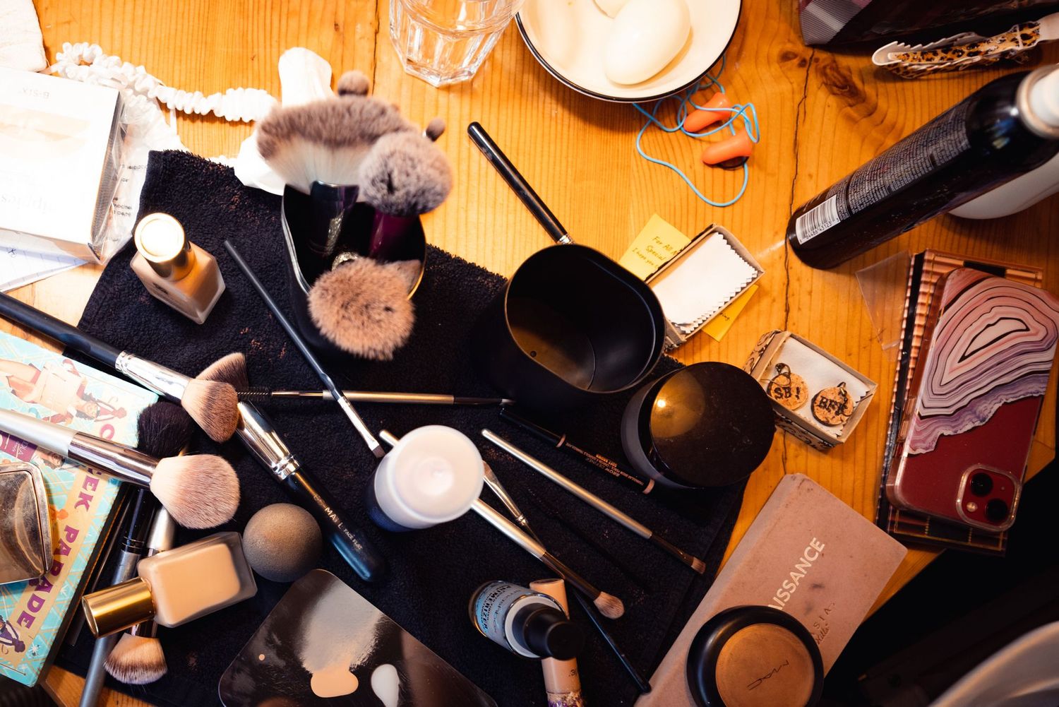 Overhead view of makeup brushes, cosmetics, and beauty tools scattered on a wooden surface.