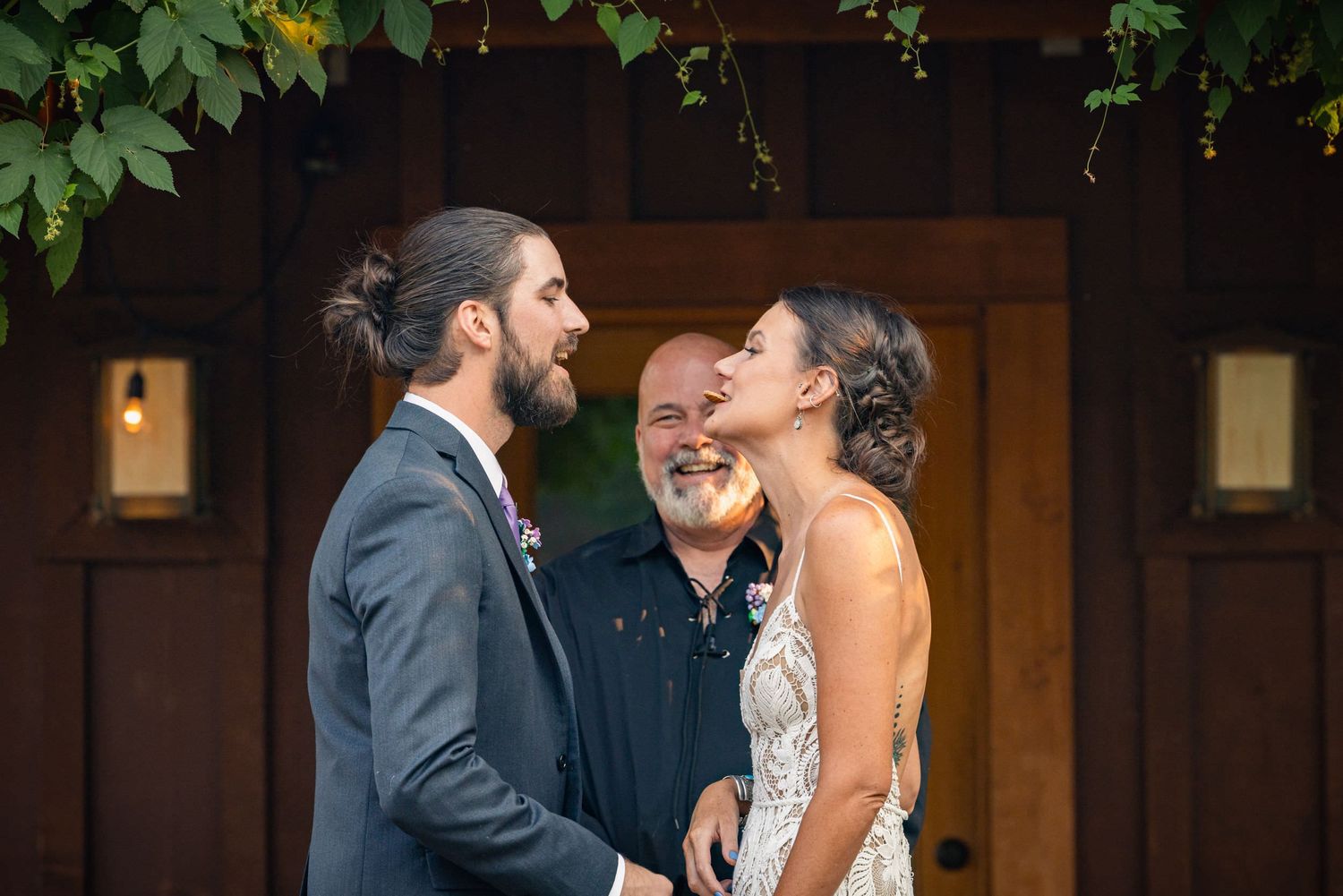 A joyful wedding ceremony with couple and officiant sharing a laugh at the altar under green foliage.