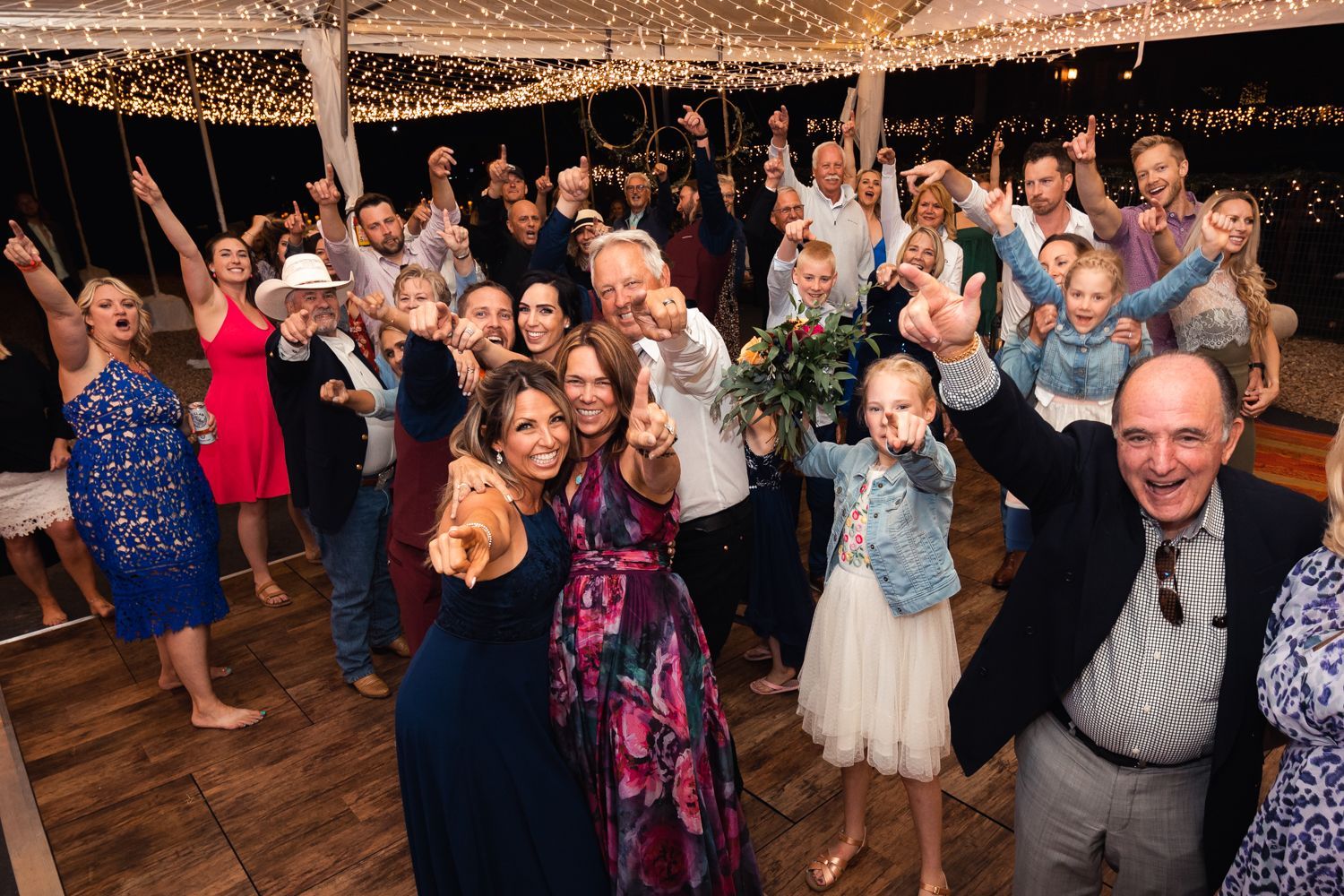 A lively wedding reception dance floor filled with celebrating guests under string lights.