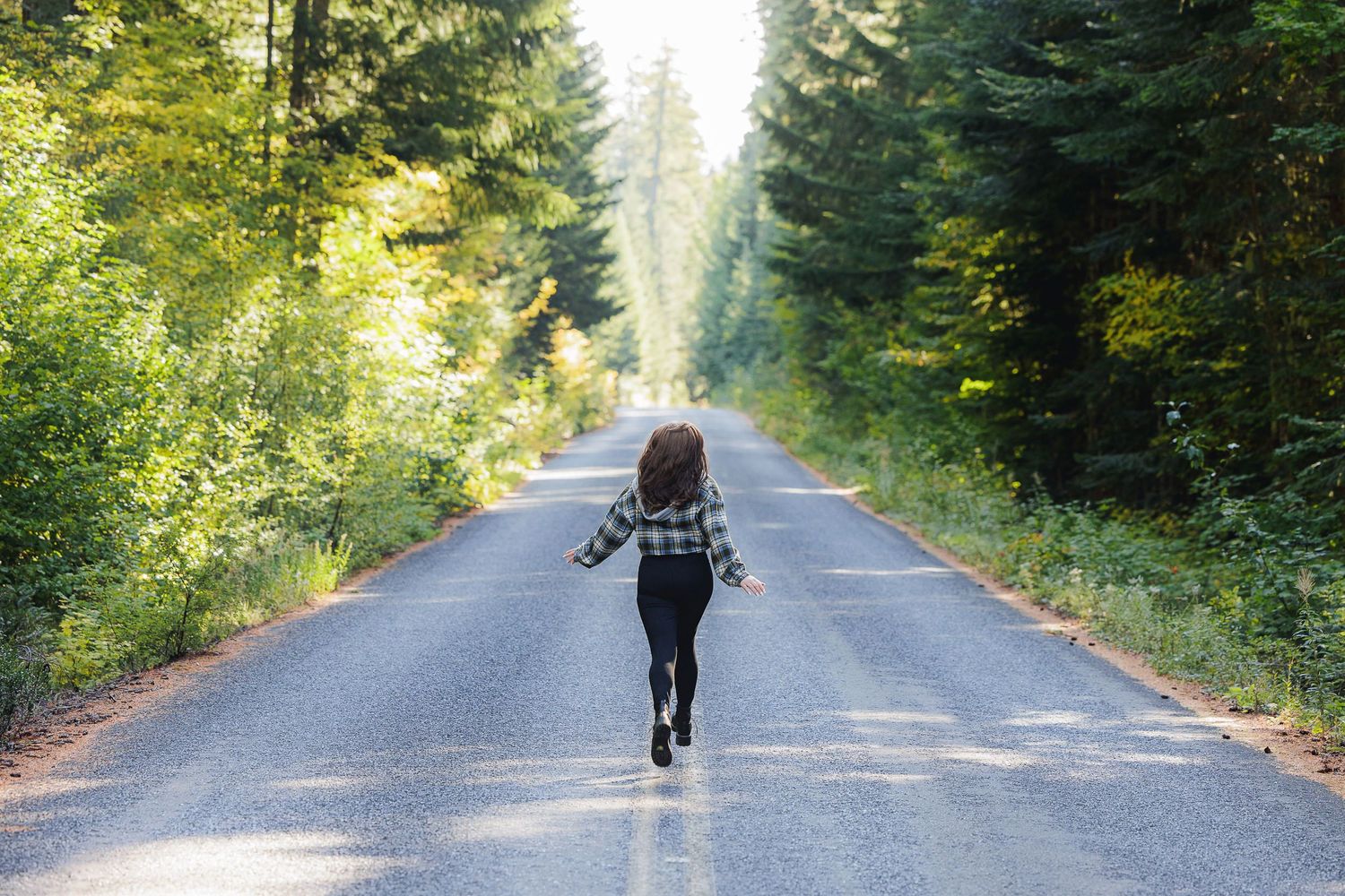 A silhouette of someone running down a tree-lined road through a dense forest.