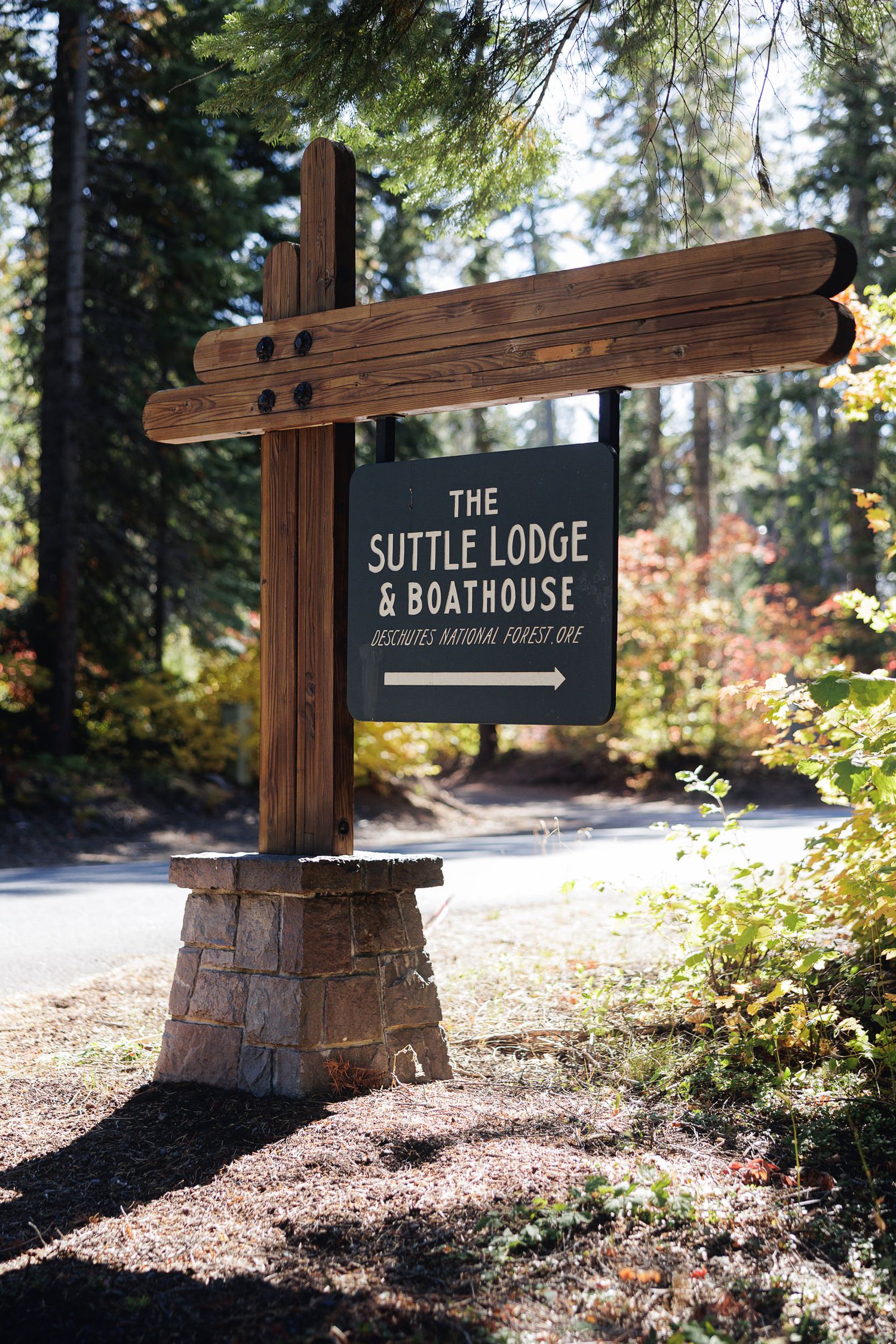 Rustic wooden sign for The Suttle Lodge & Boathouse, Deschutes National Forest, surrounded by tall pine trees.