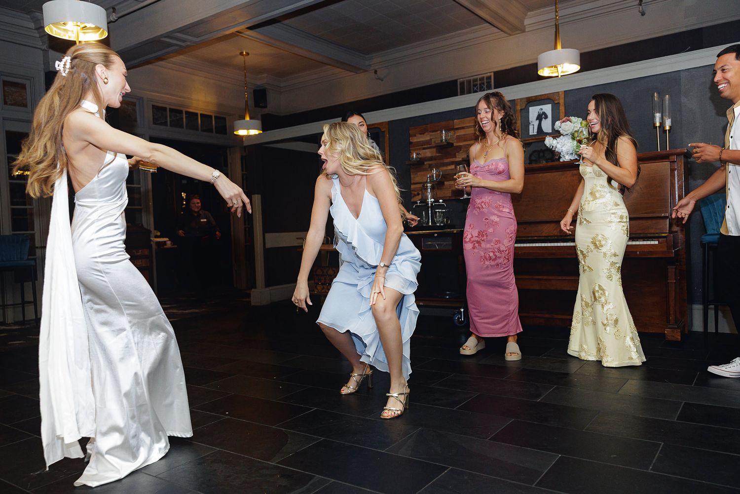 Women in formal gowns dancing at a wedding reception in an elegant venue.