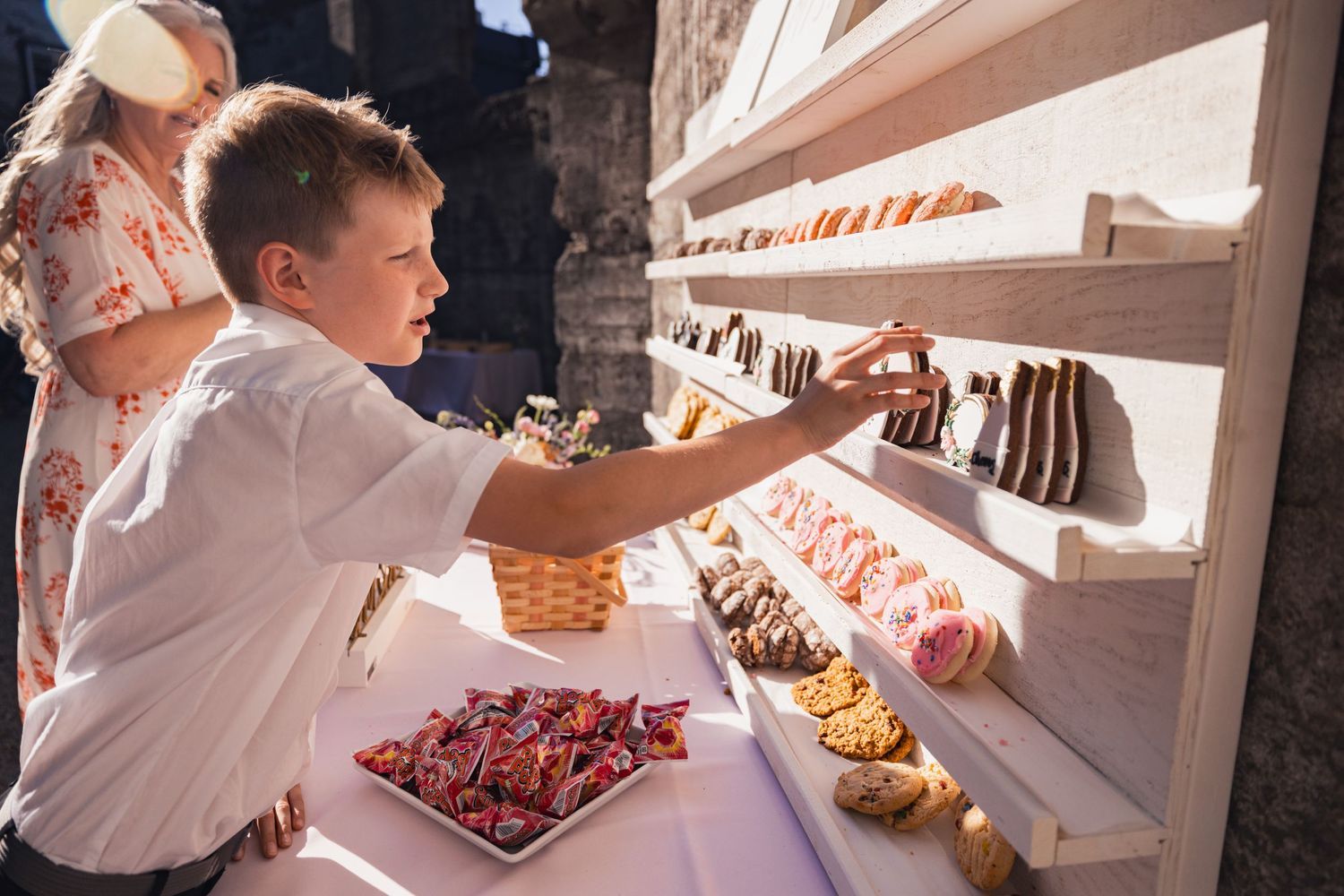 Person reaching for desserts at an elegant buffet display of colorful pastries and sweets.