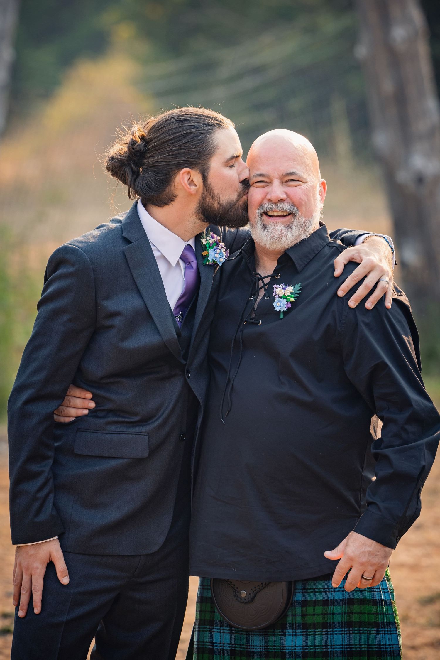 Sweet moment of affection between two people wearing matching floral boutonnieres at an outdoor event.