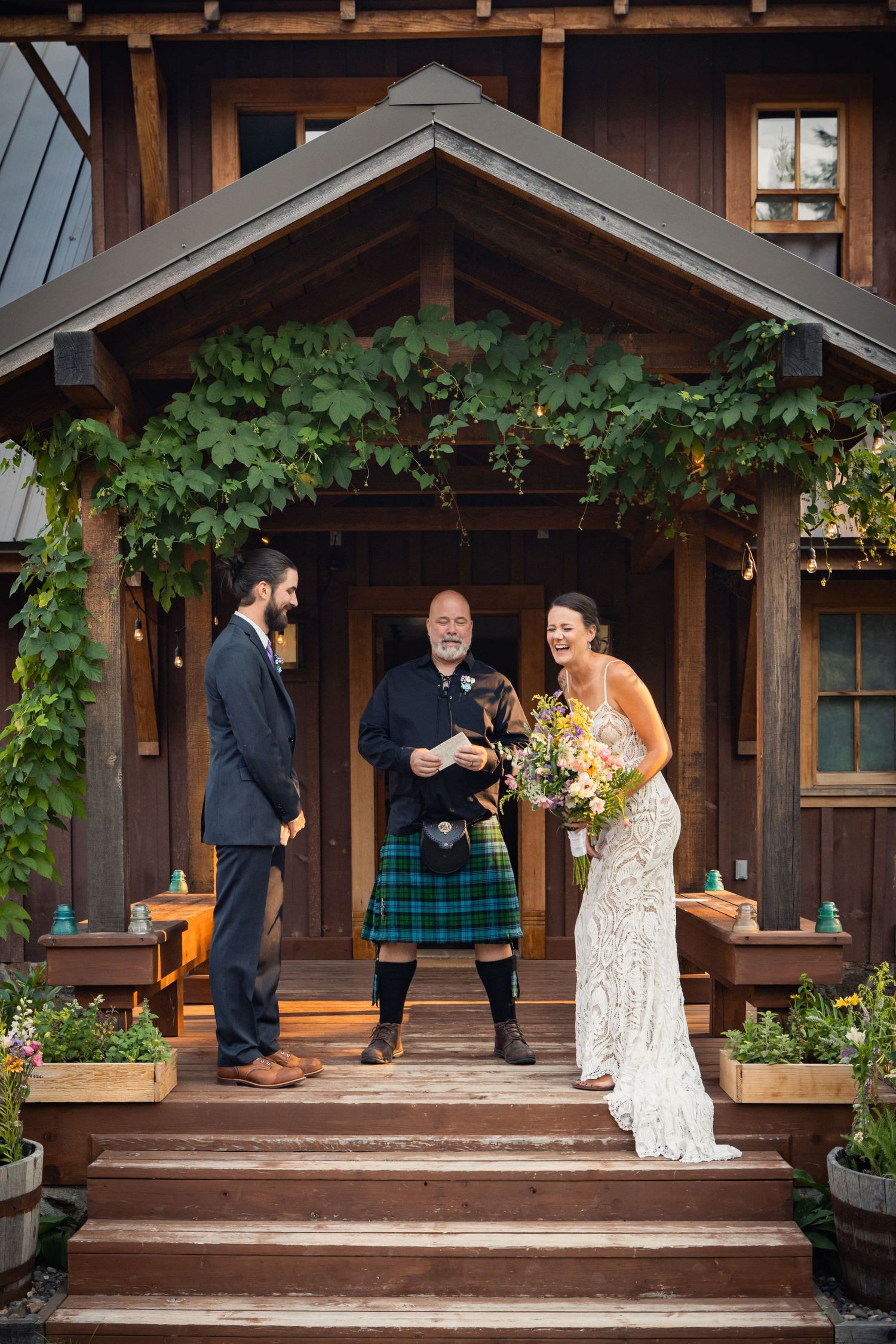 A wedding ceremony takes place on a rustic wooden porch decorated with lush green vines and florals.