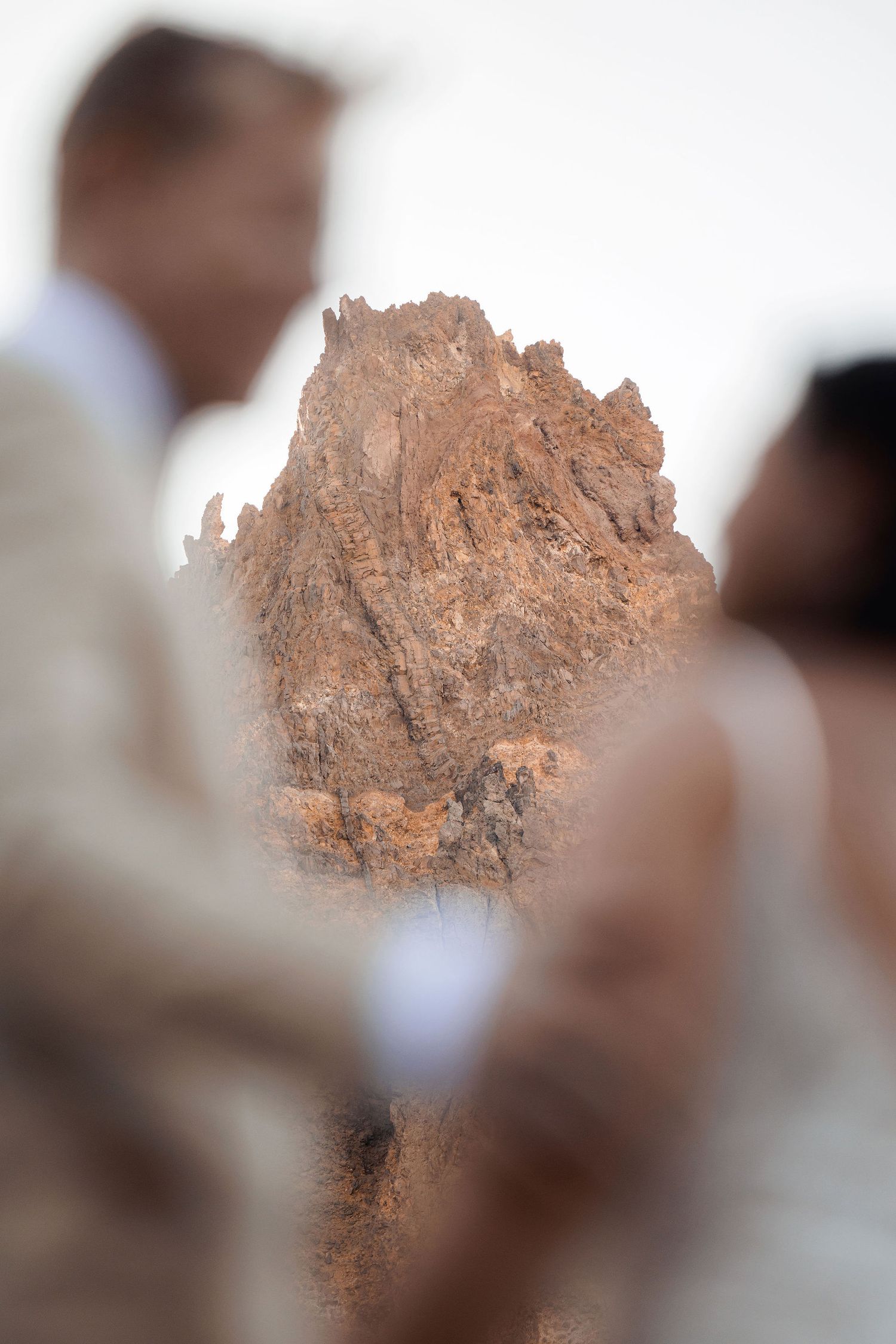 Blurred couple in the foreground frames a rugged, rust-colored rock formation in a soft, dreamy mountain wedding photo.