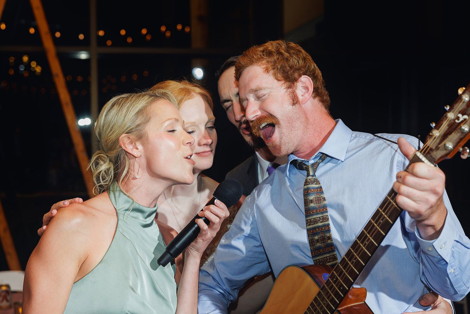 Man and woman singing together on stage, man playing acoustic guitar at a live music event.