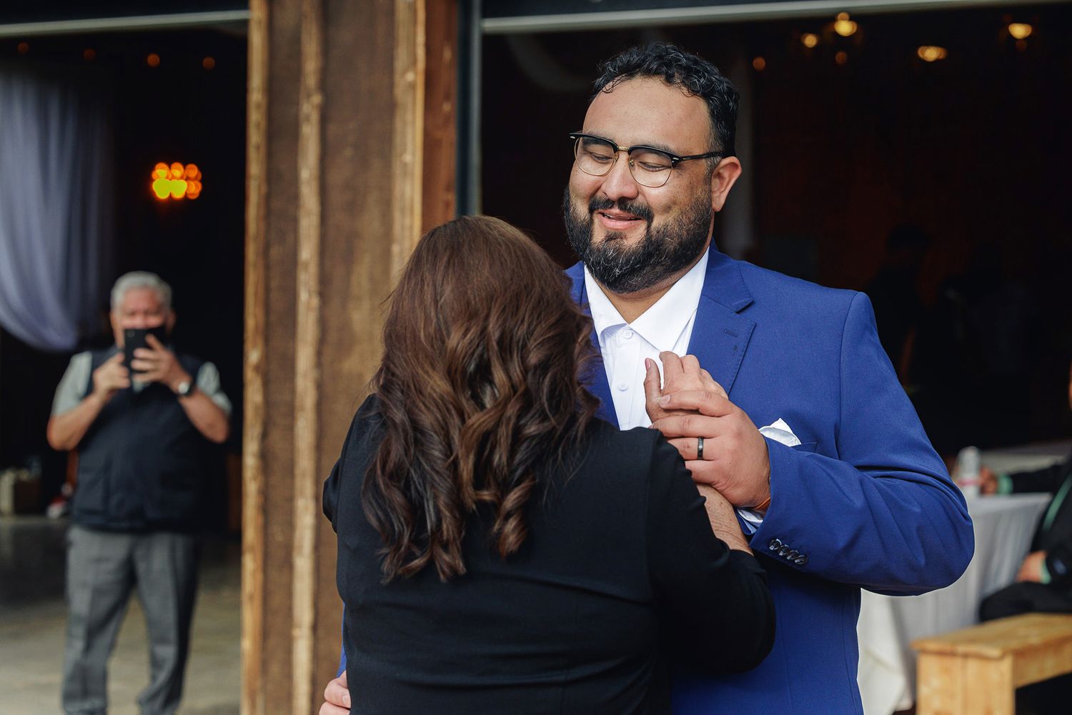 Couple sharing a dance at an indoor wedding reception, man in blue suit smiling warmly at partner.