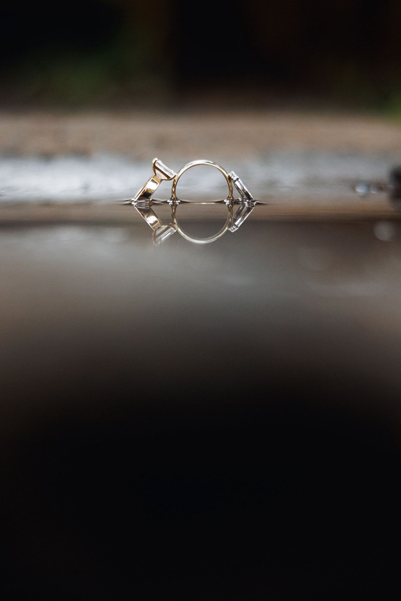 A silver diamond ring reflected on a wet surface, creating a symmetrical mirror image against a dark background.