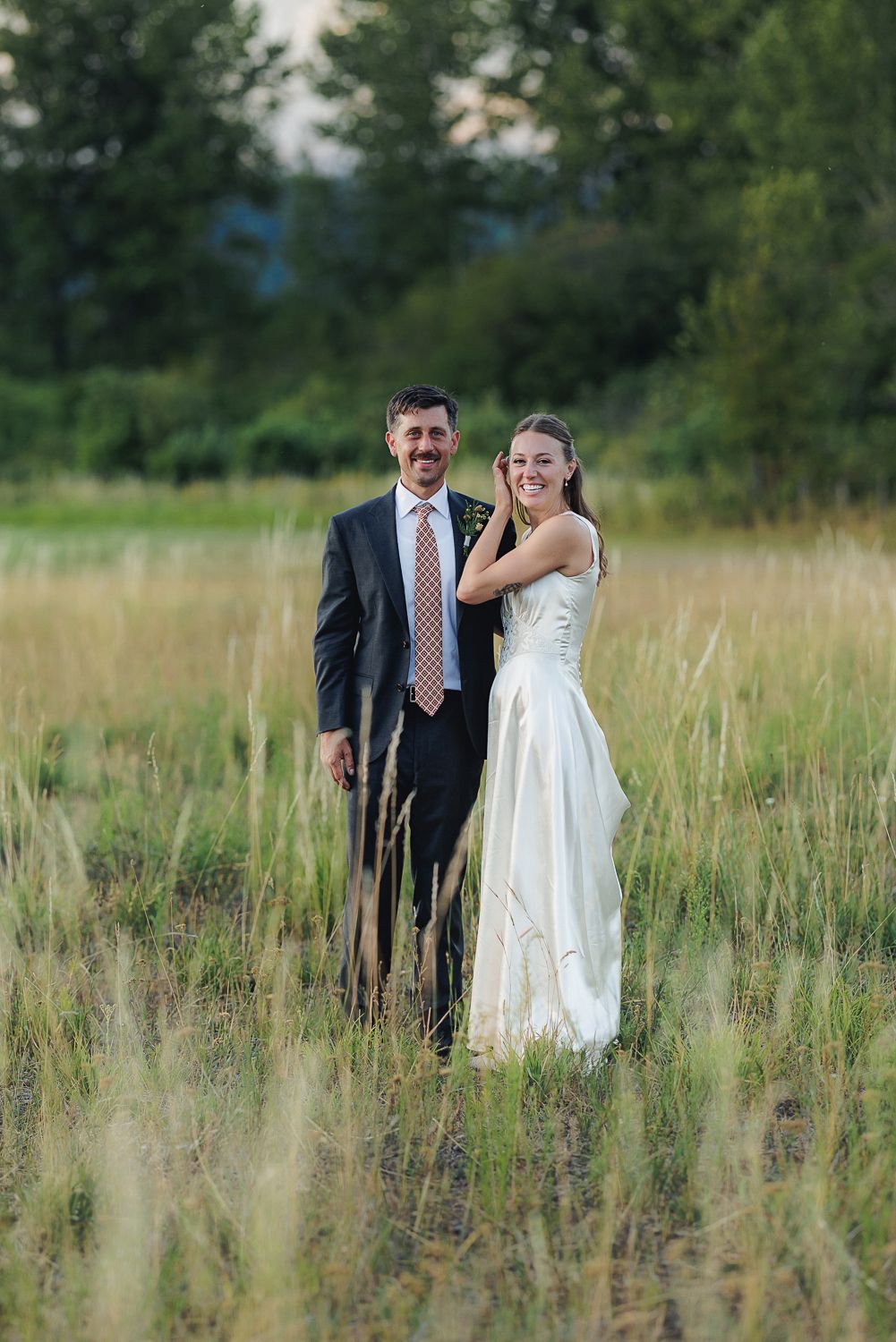 Happy couple shares a joyful moment together while standing in a tall grass field on their wedding day.