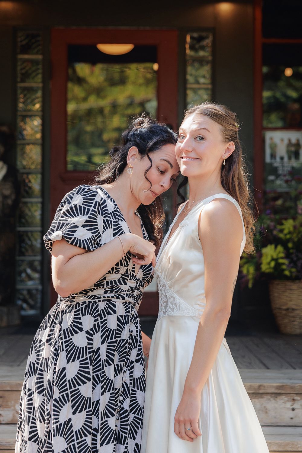 Two friends share a joyful moment on a porch, one wearing a black and white patterned dress and one in elegant white.