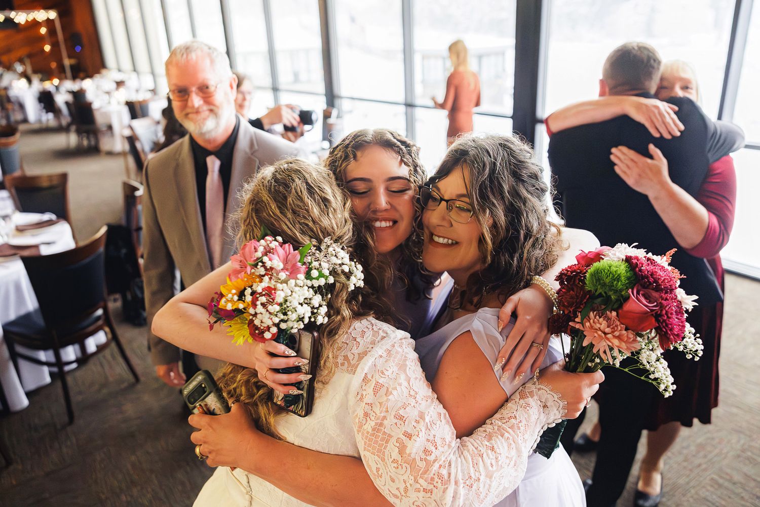 Joyful celebration with hugs and flower bouquets at an indoor reception venue.