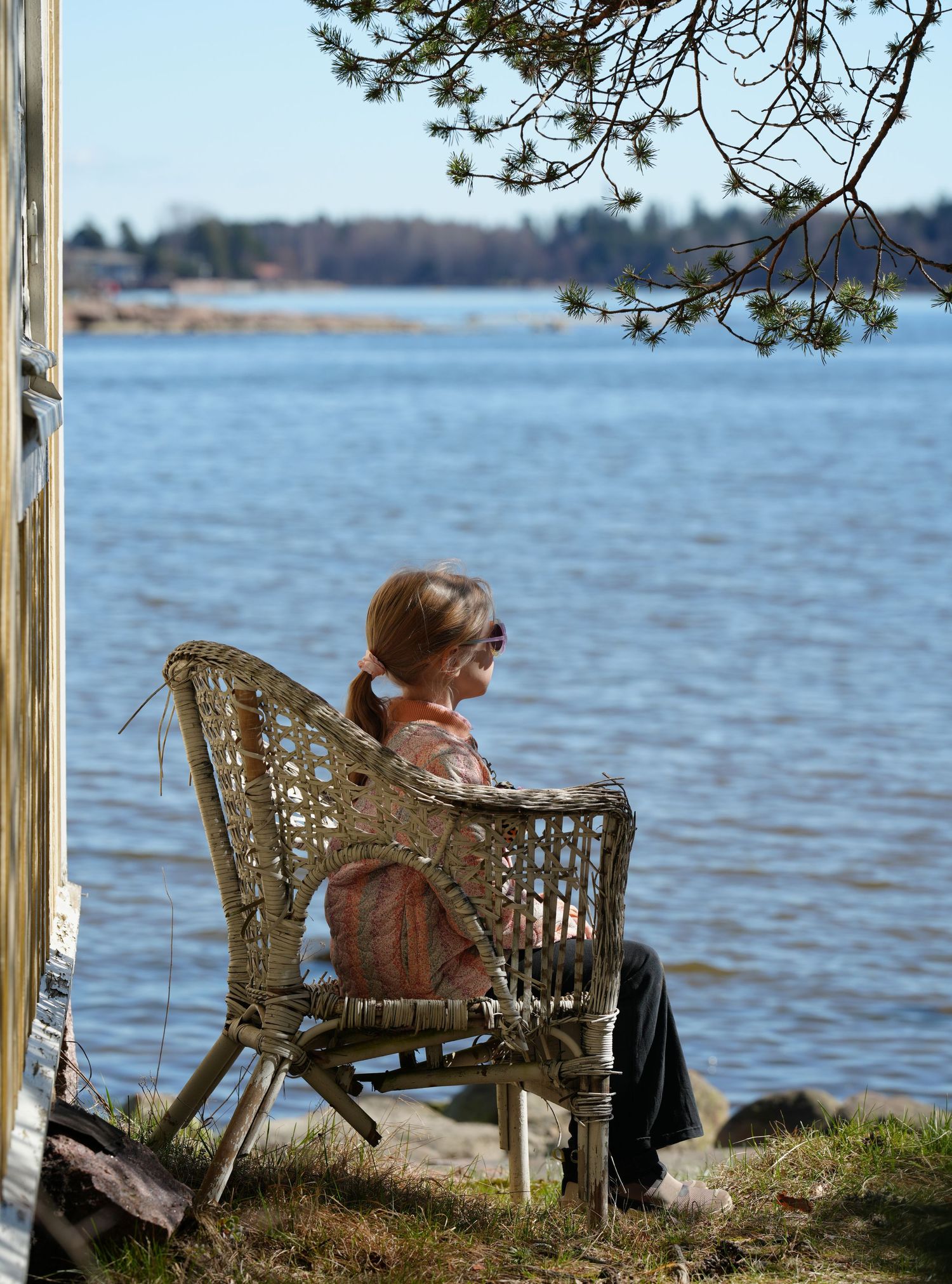 Person sitting in a wicker chair by the waterfront on a sunny day.