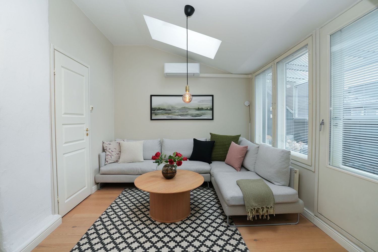 Modern living room with sectional sofa, geometric rug, and natural light from skylight and windows.