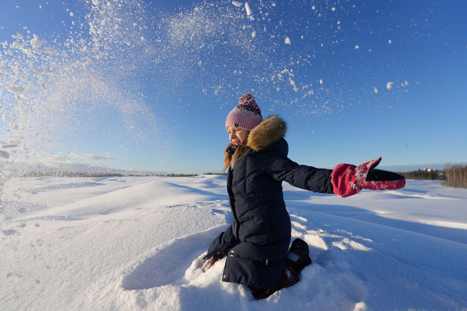 Person playing in snow throws powder into the air against bright winter sky.