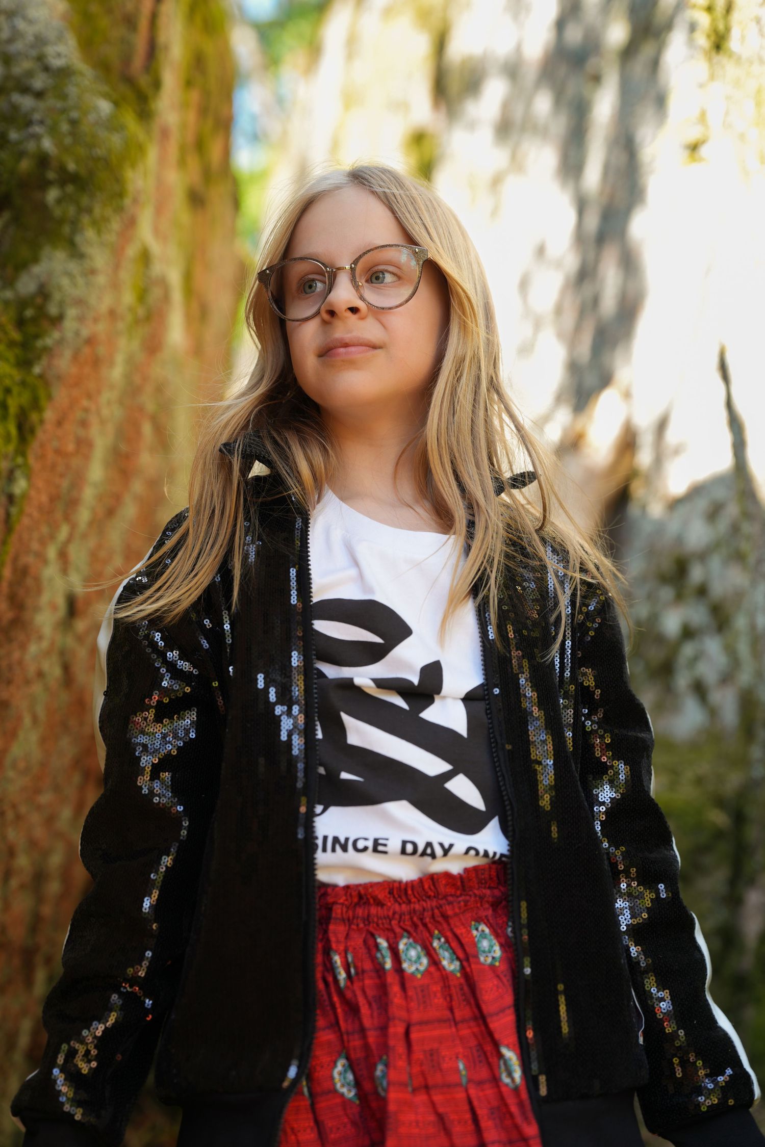 A stylish ensemble featuring a black sequined jacket, white graphic tee, and red skirt photographed in an outdoor setting.