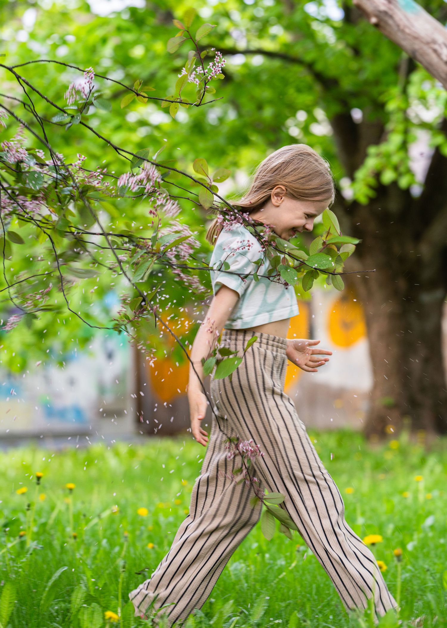 A joyful spring scene under flowering trees with striped pants and floating orange orbs in a garden setting.