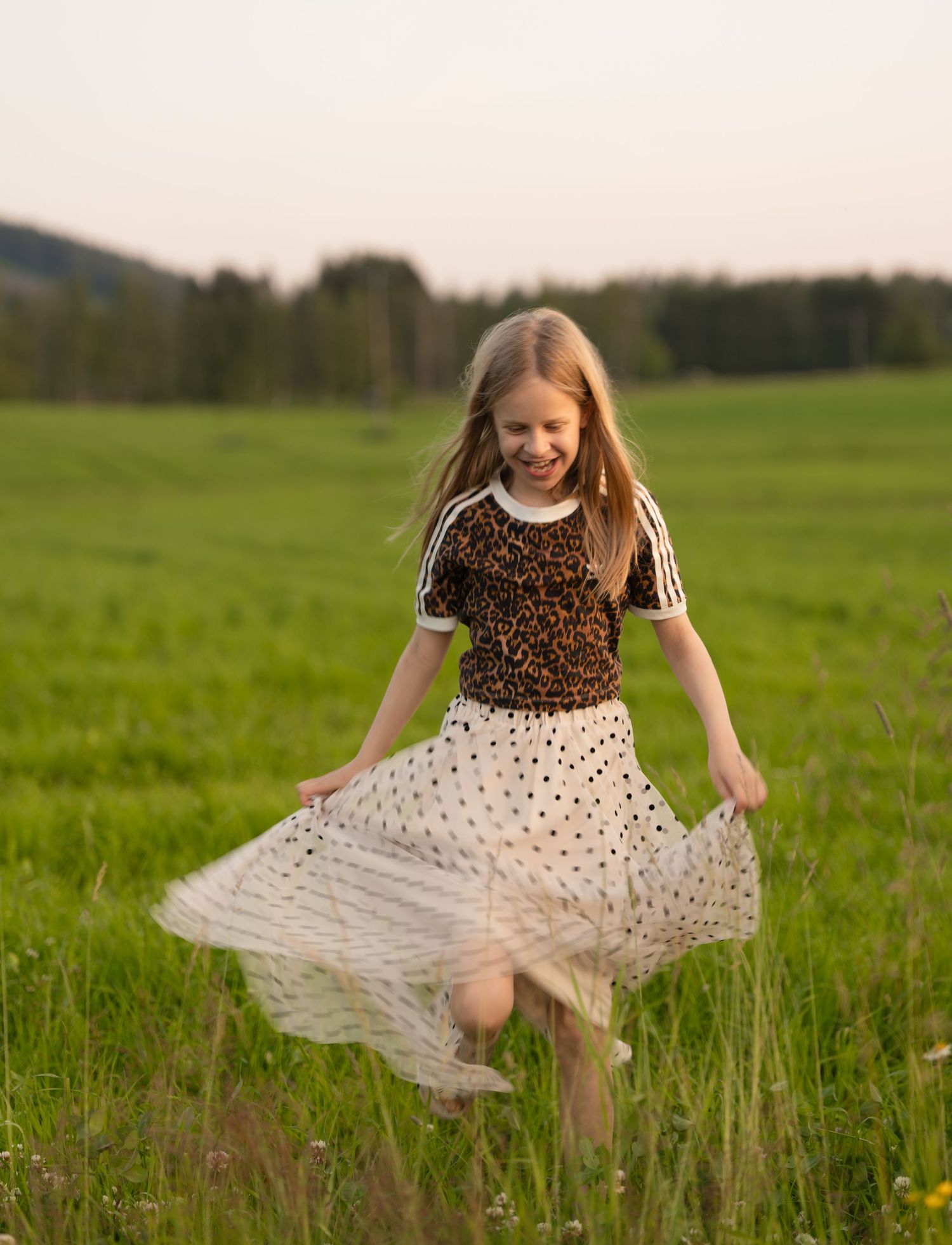 Someone in a polka dot skirt and leopard print top twirls joyfully in a green meadow at sunset.