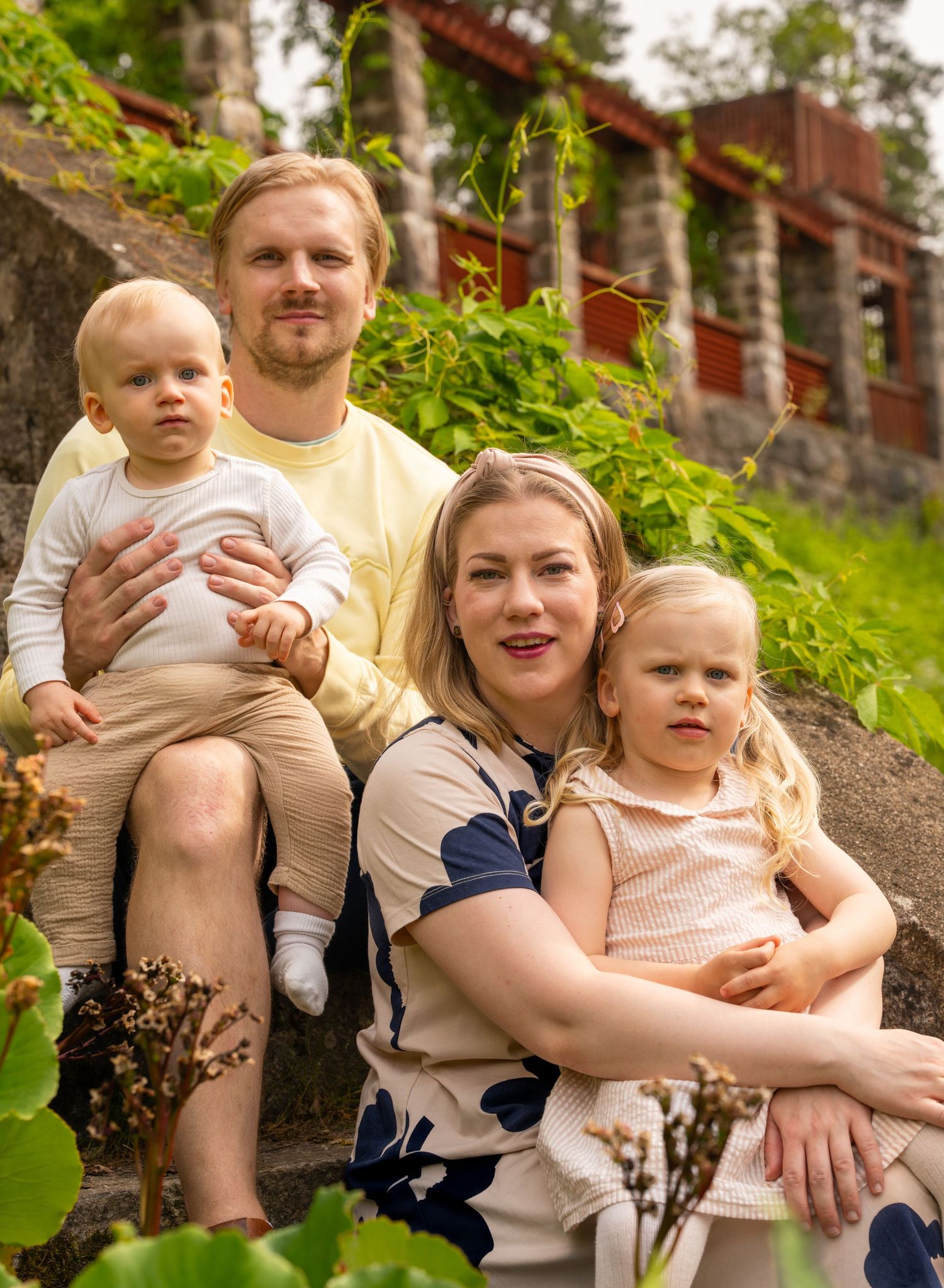 Group sitting together on rock stairs outdoors surrounded by lush greenery on a sunny summer day.