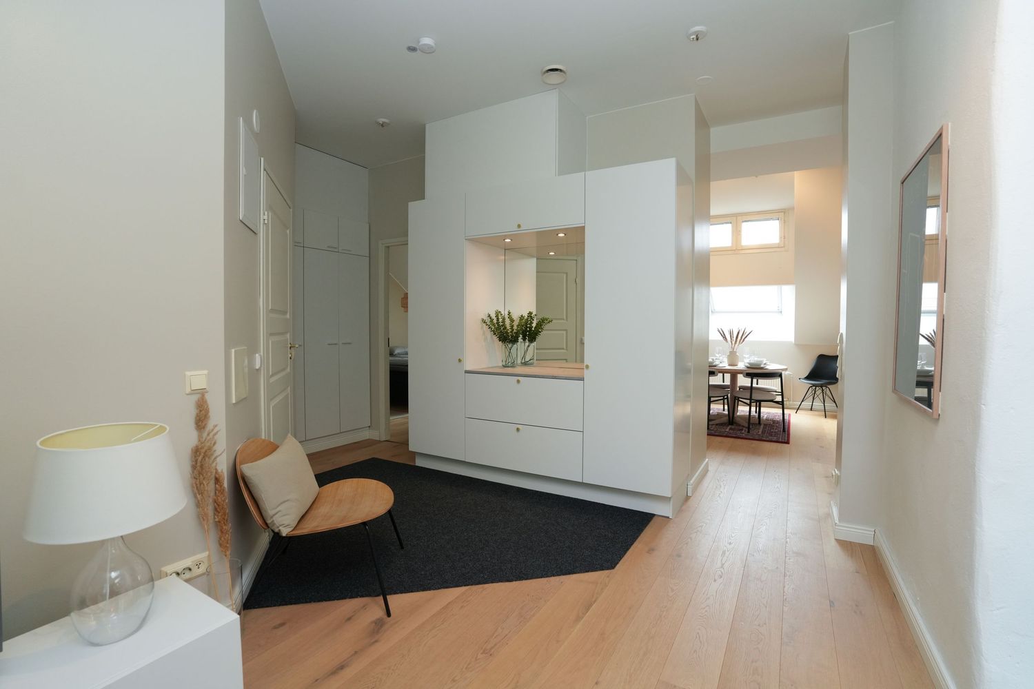 Modern minimalist hallway with white storage unit, wooden floor, and black area rug leading to dining area.