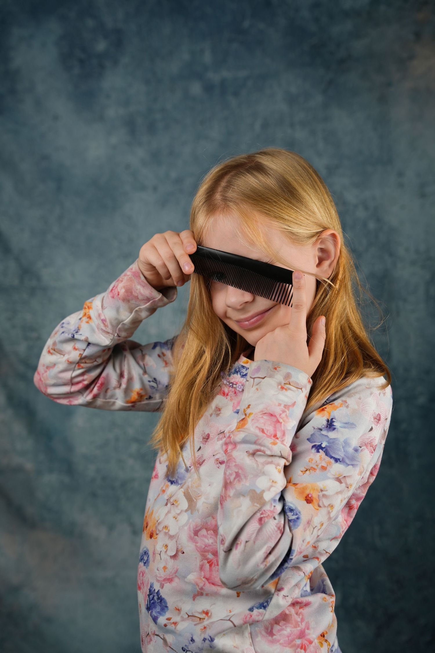 Person in floral print shirt playfully covering eyes with dark strip against blue background.