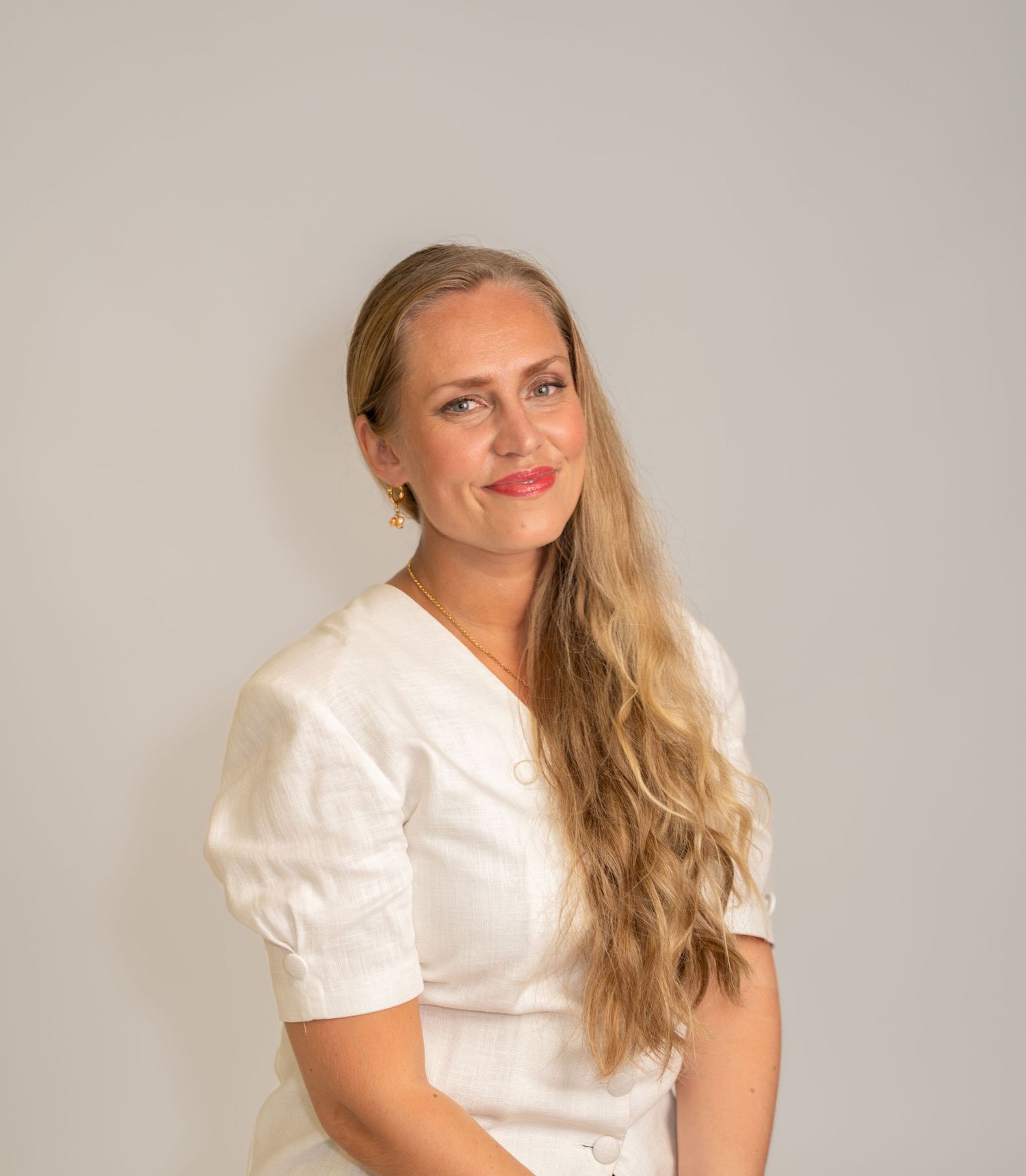 A person in a white puff sleeve top poses against a neutral background with a warm expression.