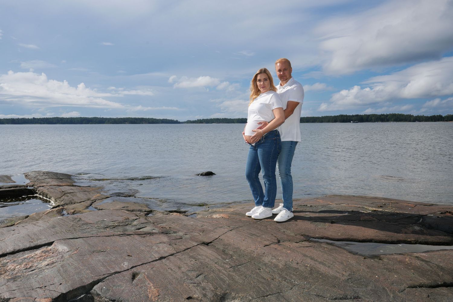 Couple standing on rocky shoreline overlooking a lake on a cloudy day.