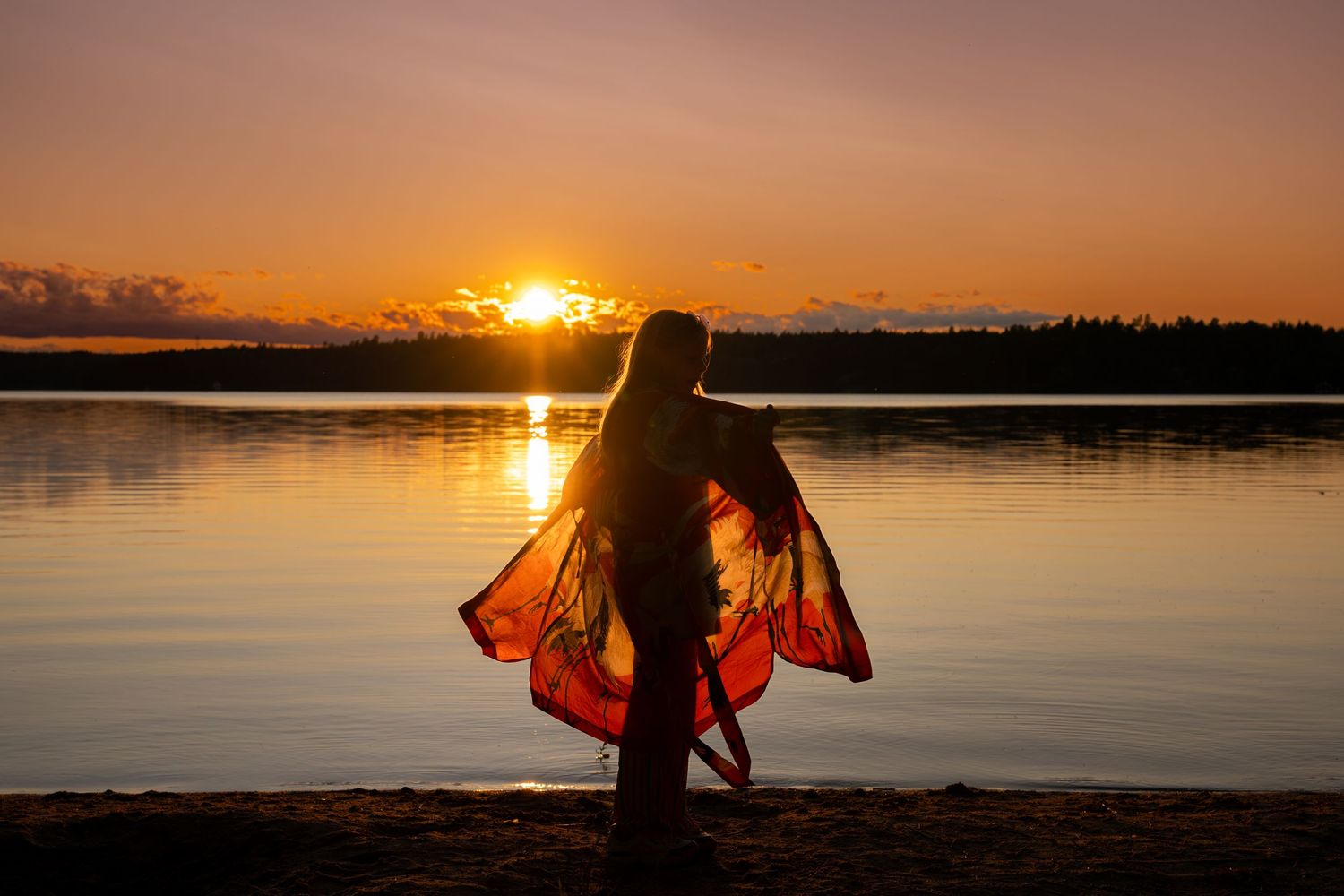 Two figures stand in silhouette against a golden sunset over a tranquil lake.