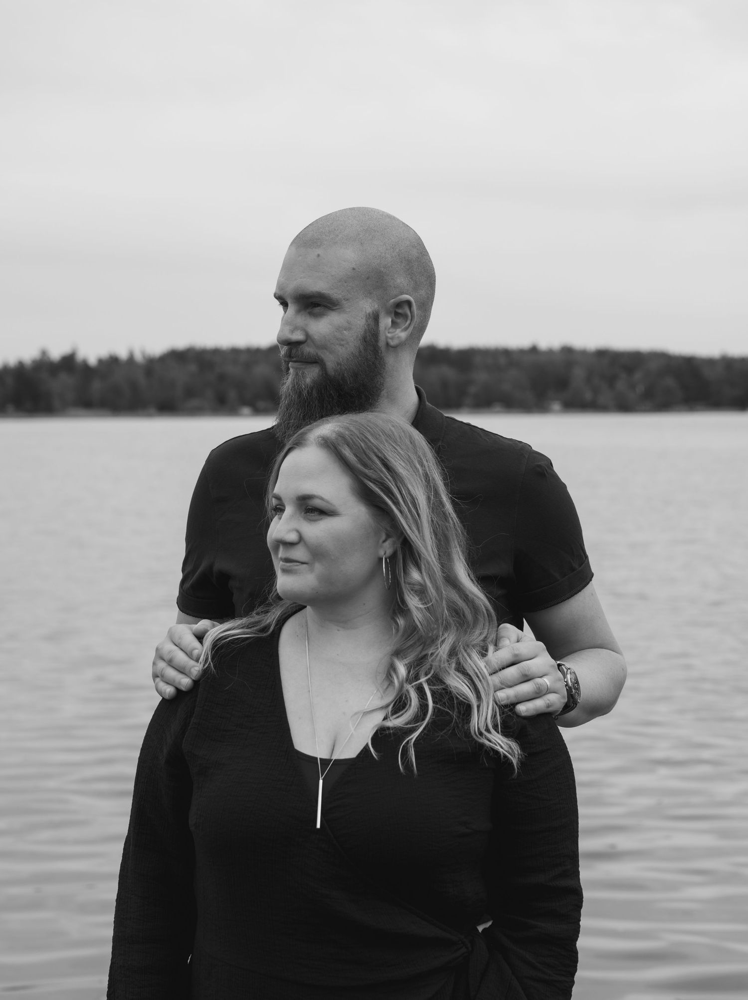 A tender black and white photo series showing an affectionate couple embracing by a serene lakeside against a natural backdrop.