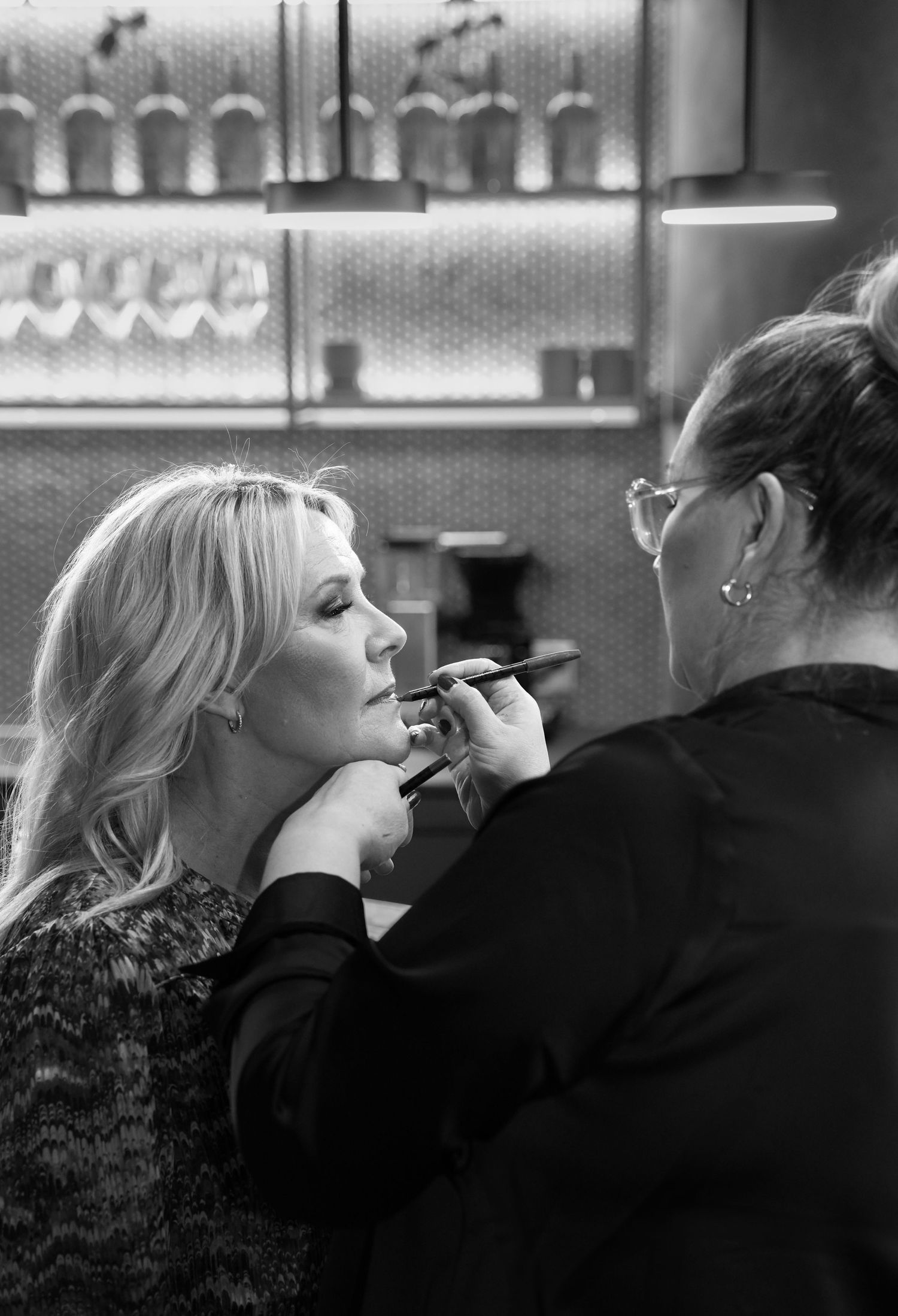 Professional makeup artist applying cosmetics in a dimly lit bar or salon setting.