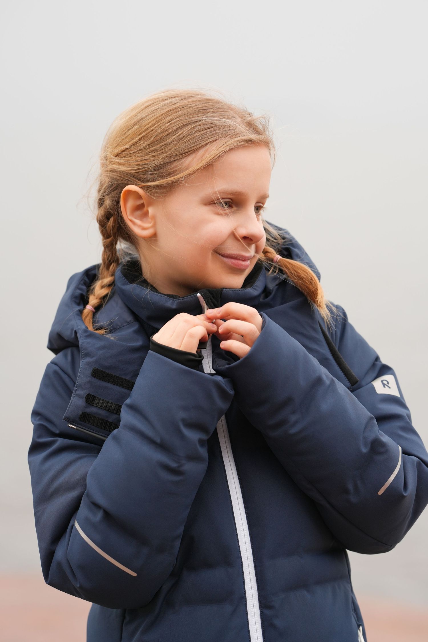 Young person in navy winter coat with braided hair smiling outdoors.