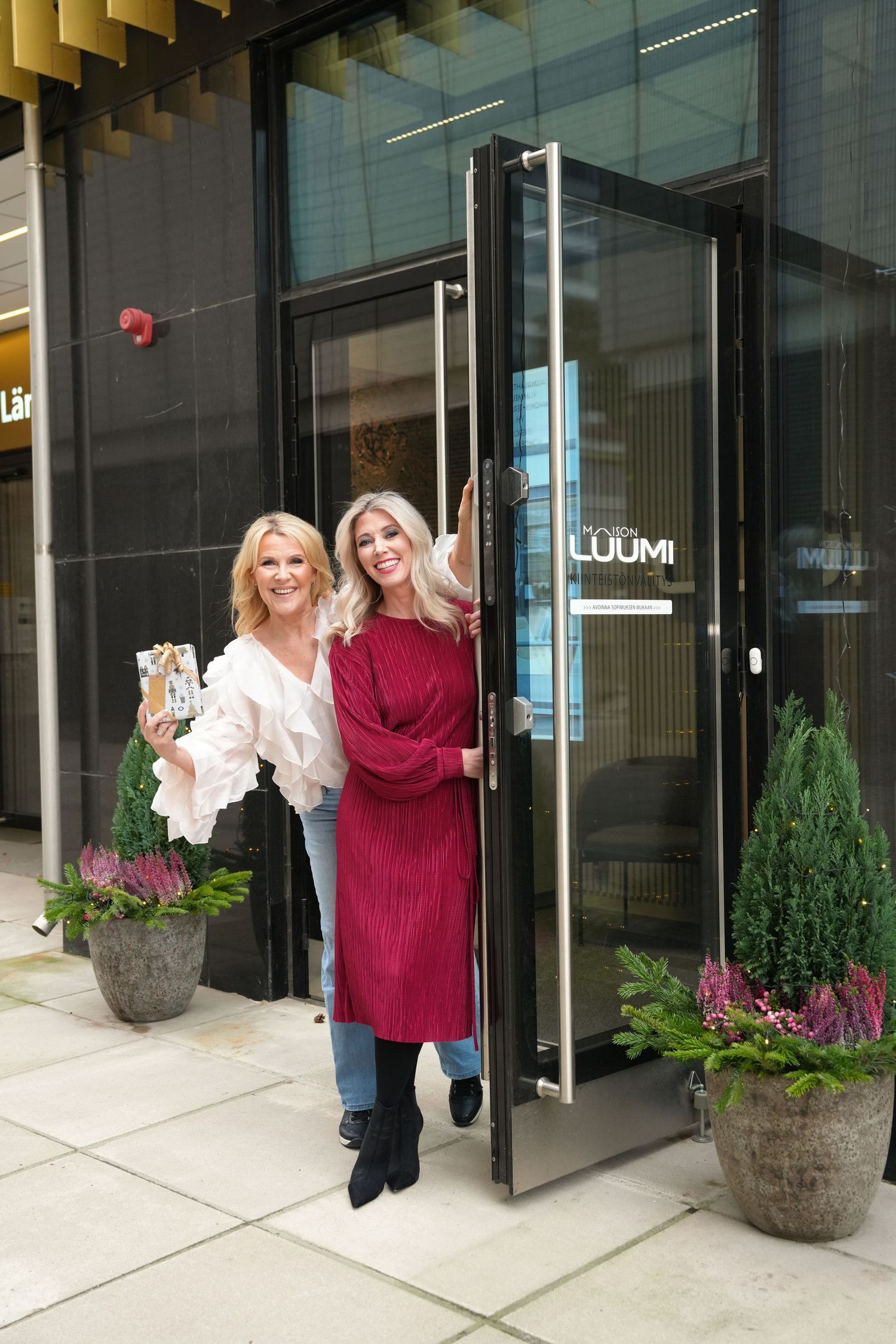 Two people in contrasting white and red outfits standing outside modern building entrance.