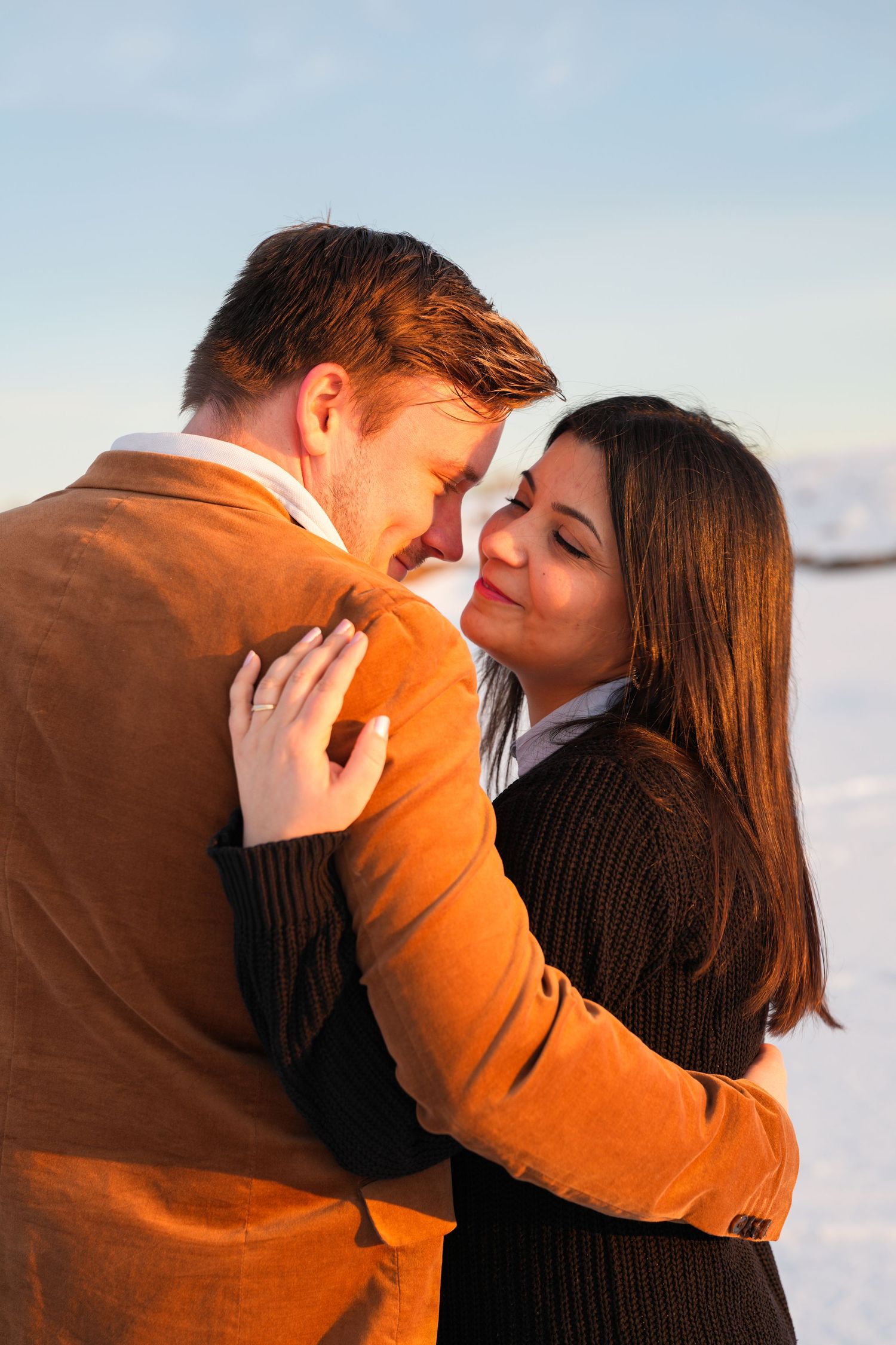 Romantic couple in winter clothing sharing an intimate moment against snowy backdrop.