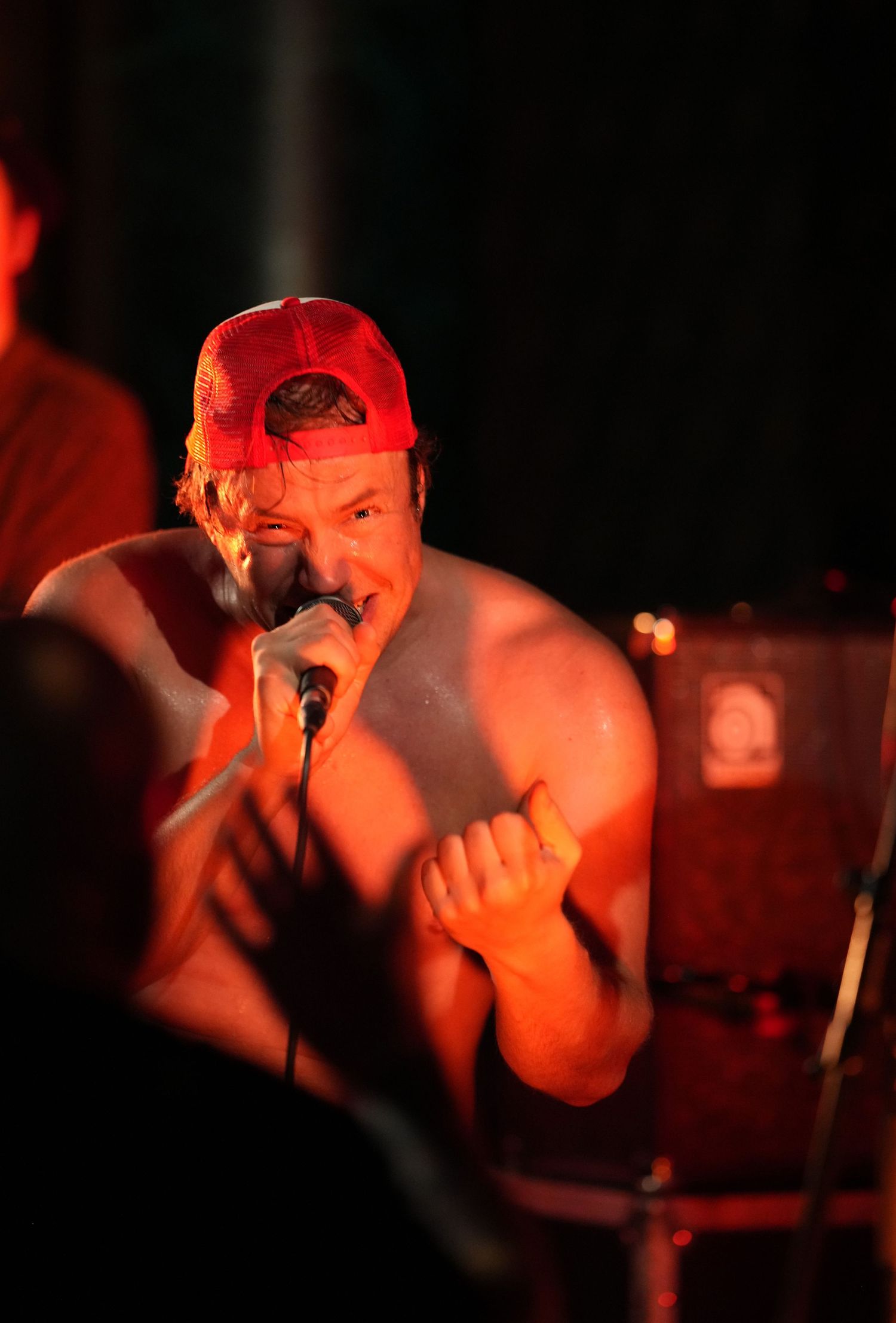 Performer singing passionately into microphone under red stage lighting.