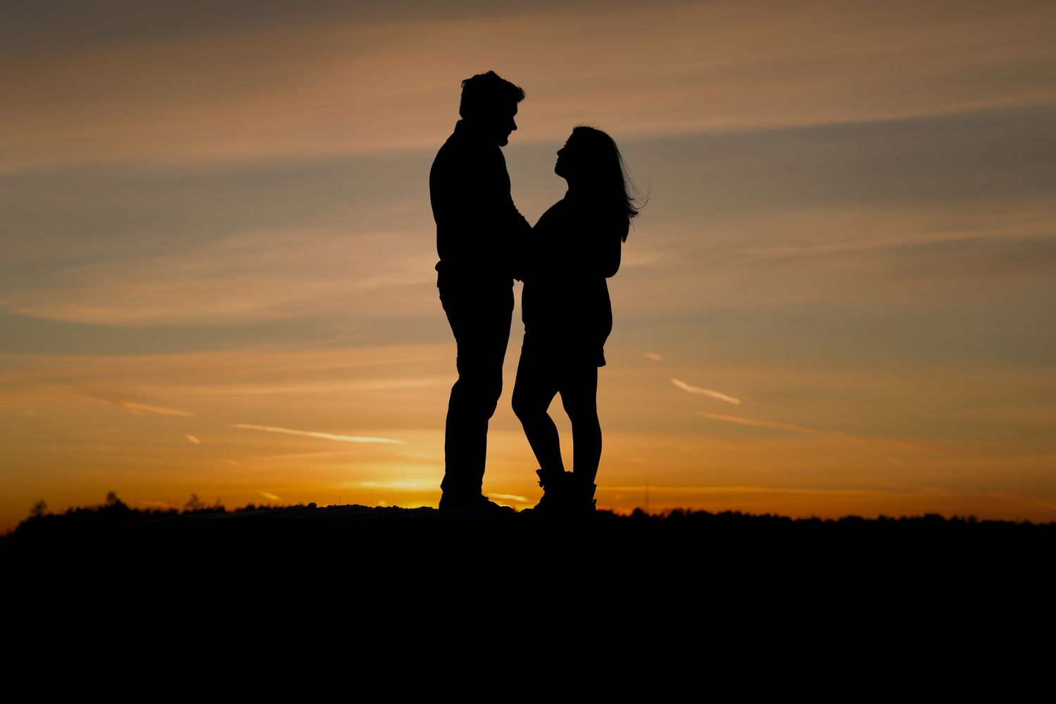 Romantic silhouette of two people standing close together at sunset.
