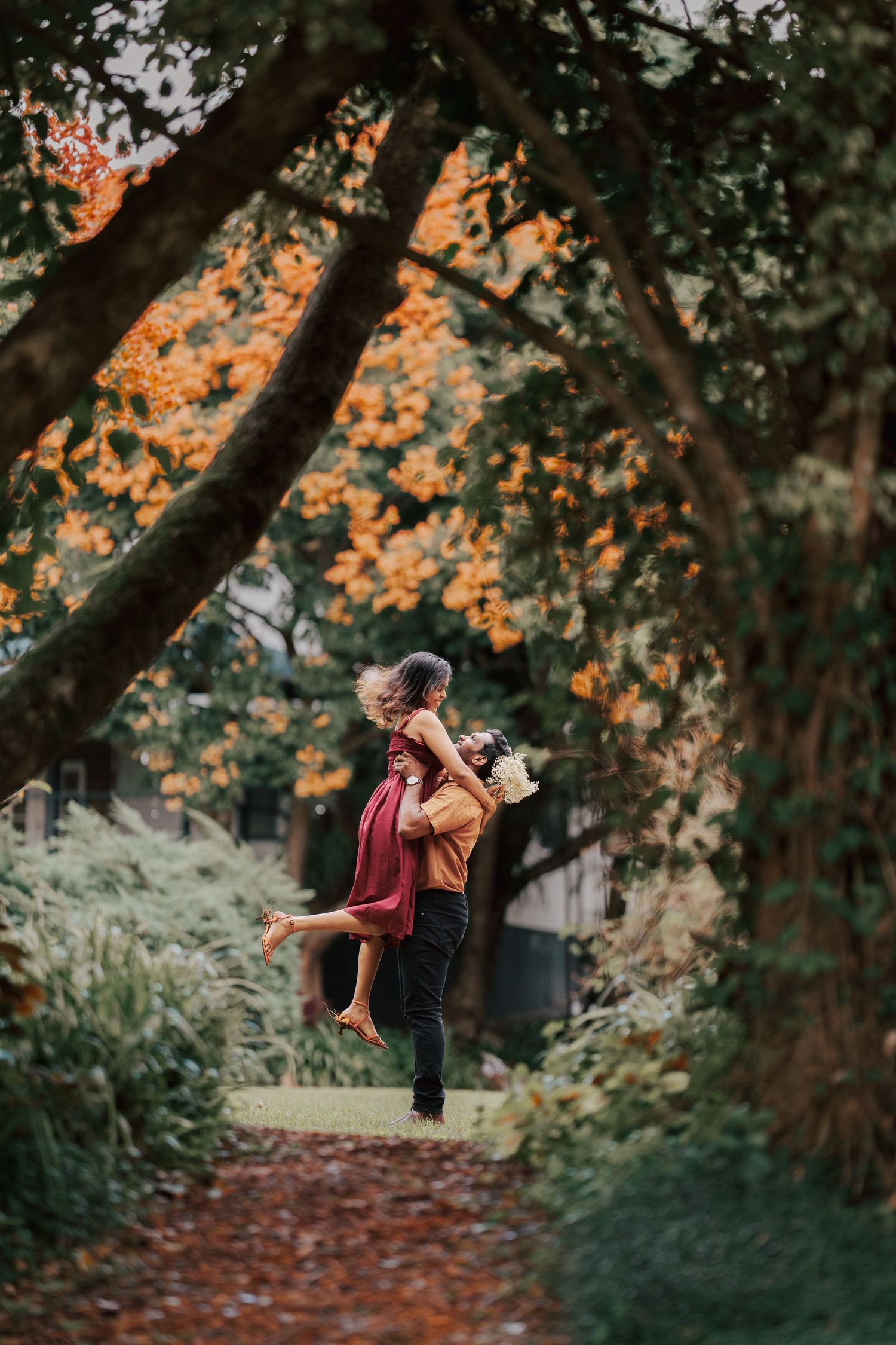 A romantic autumn scene along a wooded path with warm orange foliage glowing in the background.