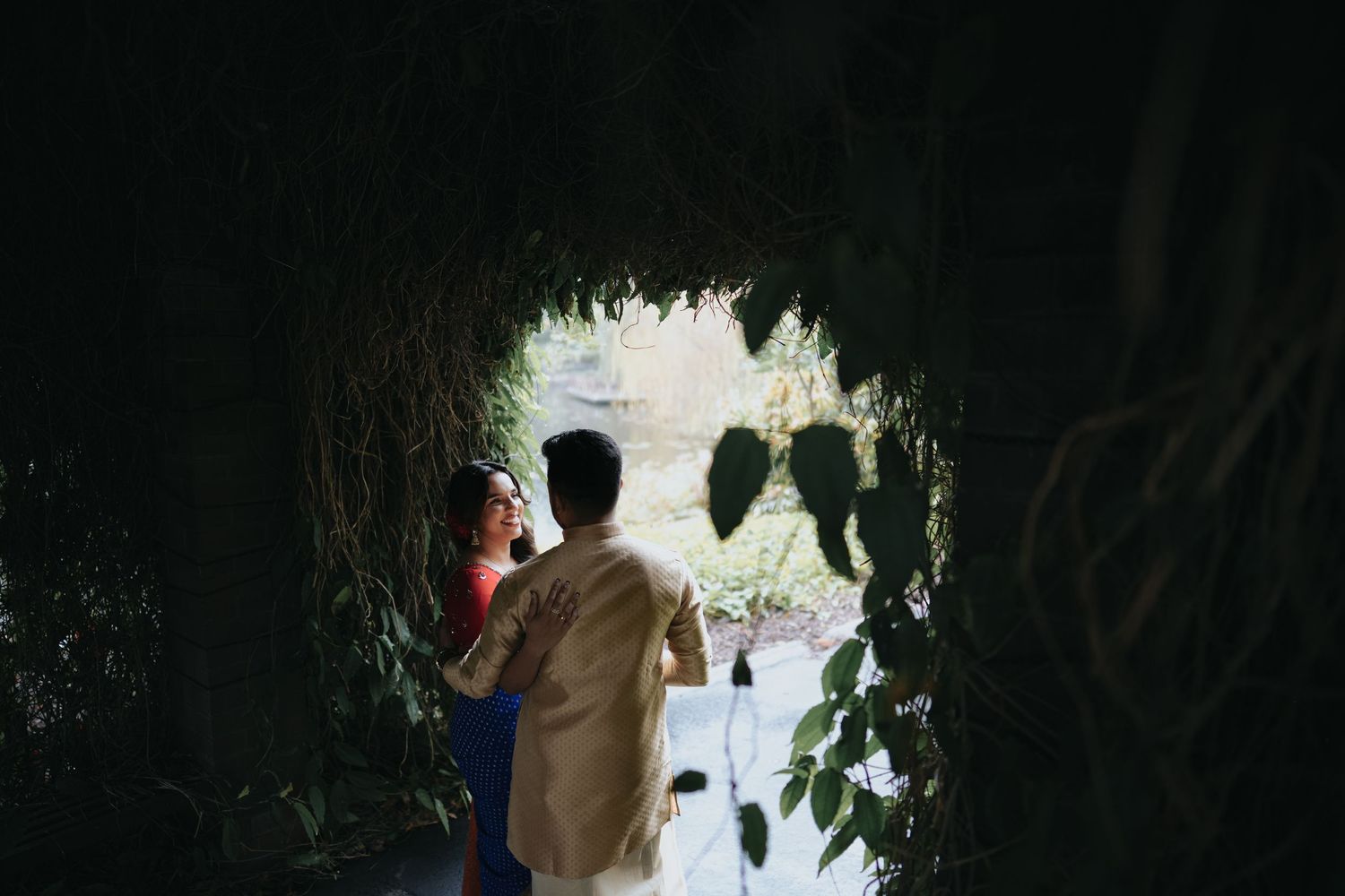 Silhouetted couple framed by natural cave archway with greenery.