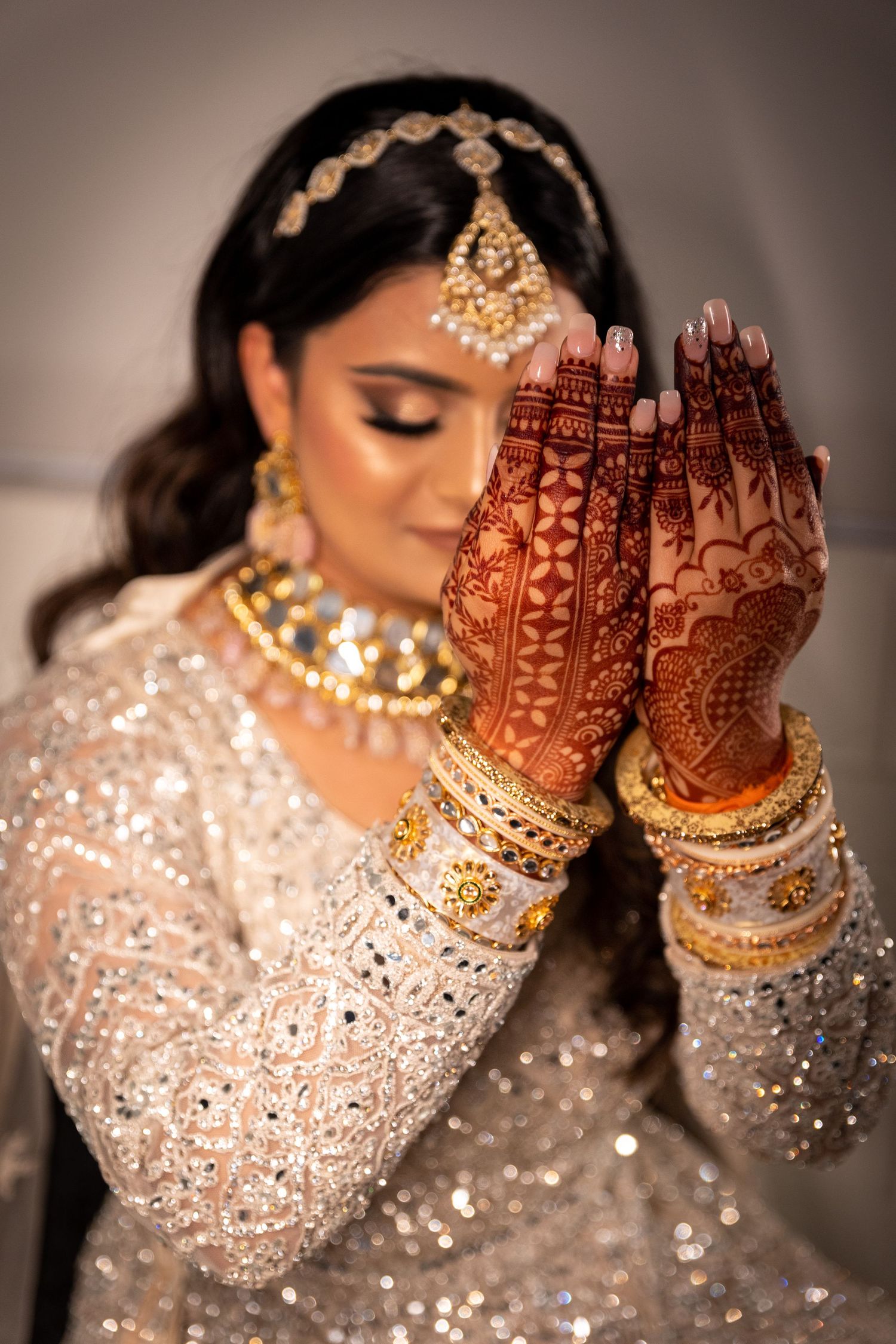Intricate henna designs on hands adorned with gold bangles and jewelry against sparkly outfit.