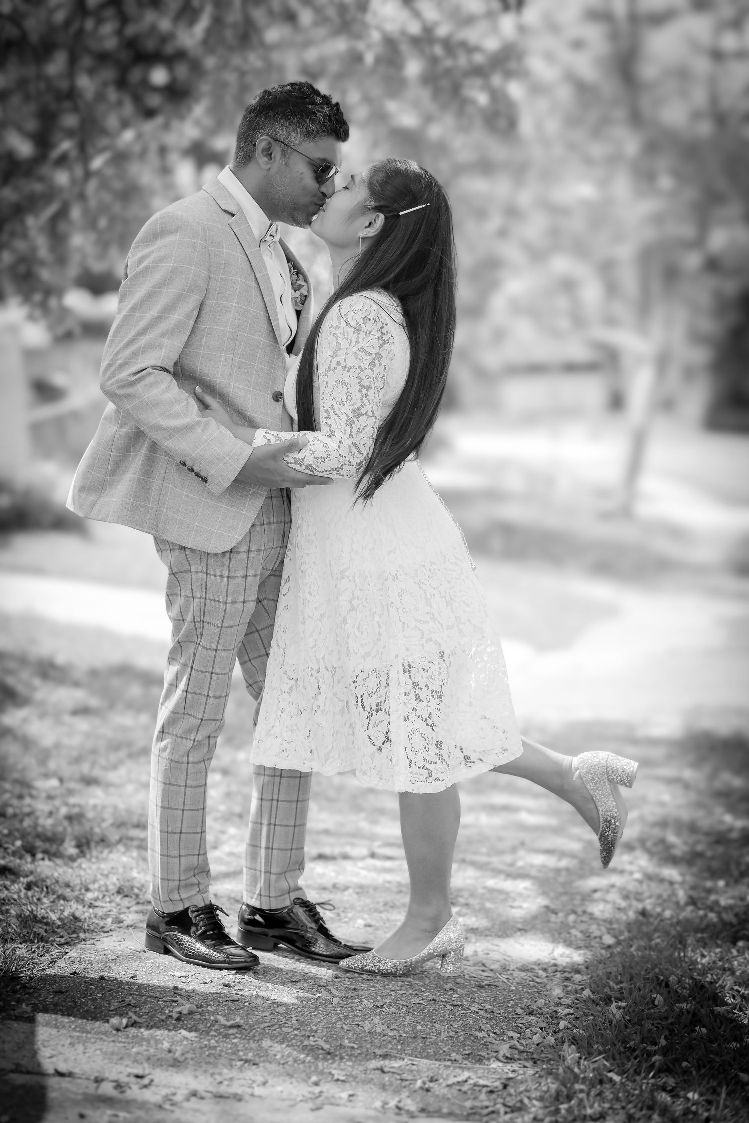 A romantic black and white photo showing a tender kiss between a couple, with the bride lifting her foot in a classic pose.